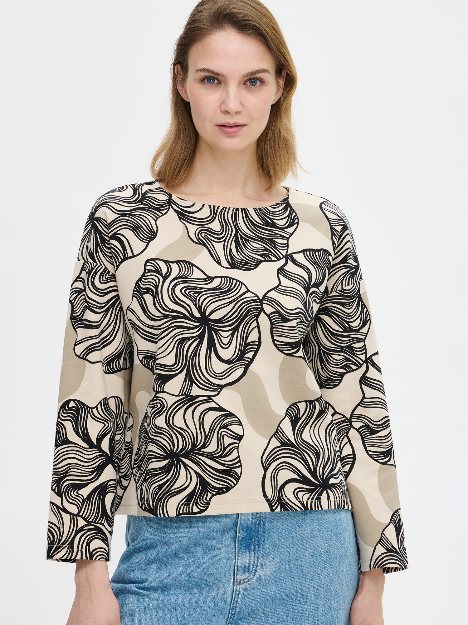 The Kosmo patterned blouse for women with a boat neckline, dropped shoulders, and full-length sleeves and side slits at the hem. On a model, close-up.