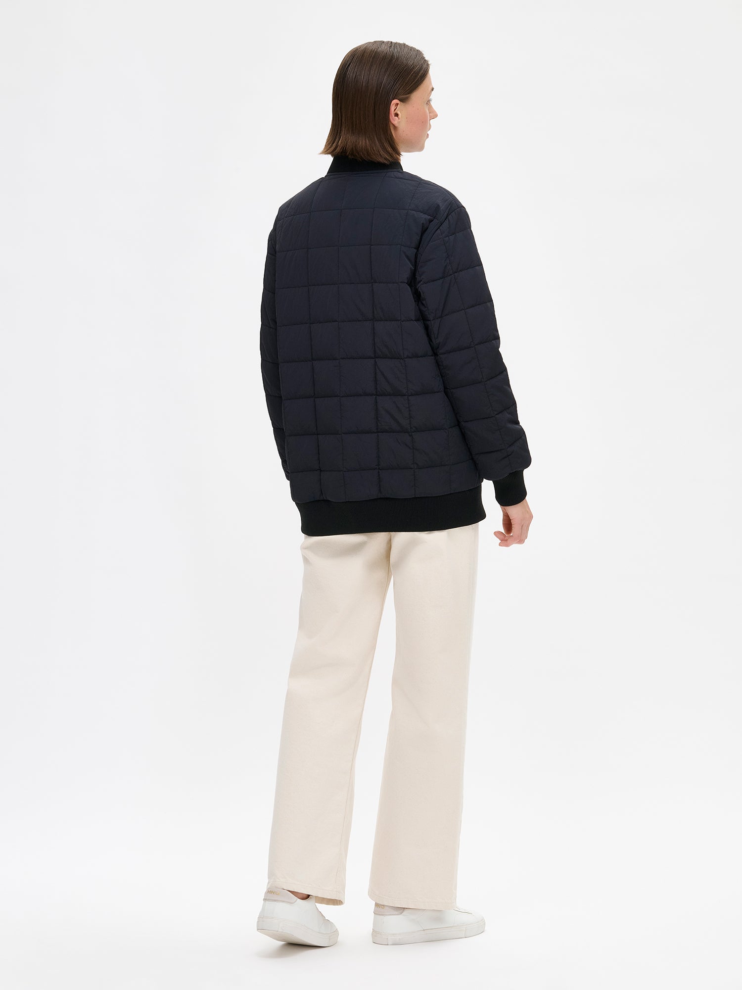 Nanso MERJE Quilted Bomber Jacket in Black features a lightweight Sorona -insulation, ribbed knit detailing at the neckline, cuffs, and hem. Dropped shoulders create a relaxed, contemporary silhouette. Photographed on a model with jeans on, from the back.
