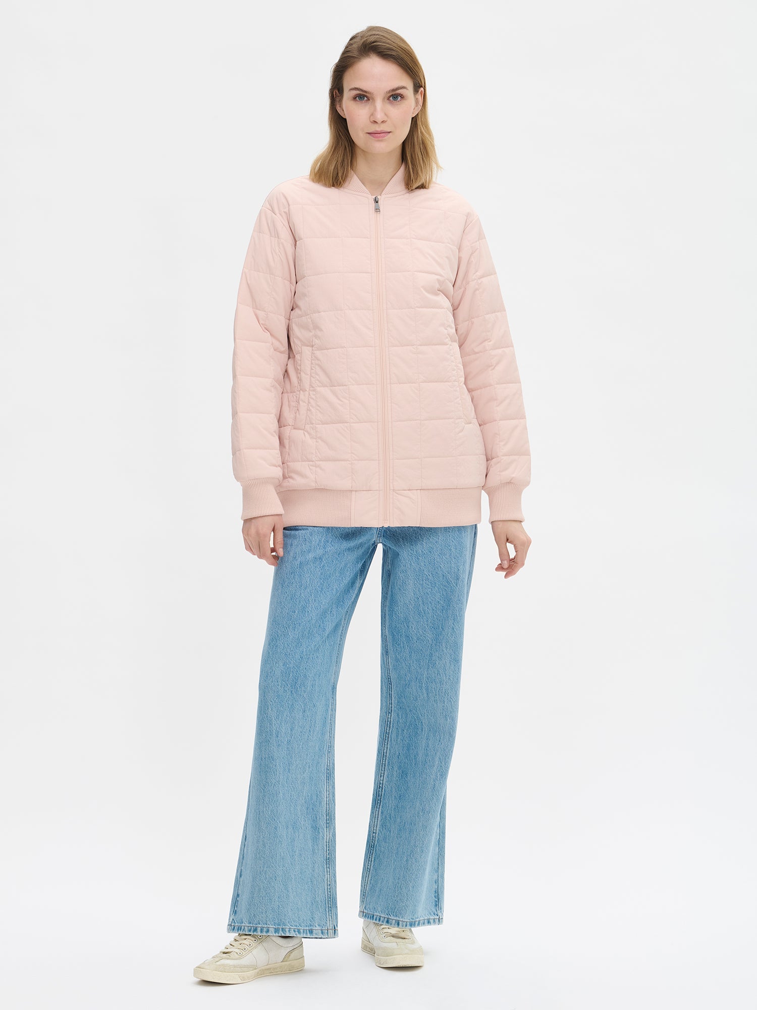 Nanso MERJE Quilted Bomber Jacket in Light Rose features a lightweight Sorona -insulation, ribbed knit detailing at the neckline, cuffs, and hem. Dropped shoulders create a relaxed, contemporary silhouette. Photographed on a model with jeans on, jacket closed.