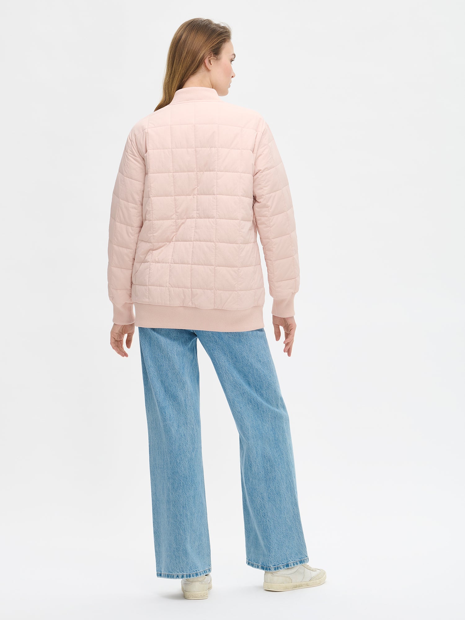 Nanso MERJE Quilted Bomber Jacket in Light Rose features a lightweight Sorona -insulation, ribbed knit detailing at the neckline, cuffs, and hem. Dropped shoulders create a relaxed, contemporary silhouette. Photographed on a model with jeans on, from the back.