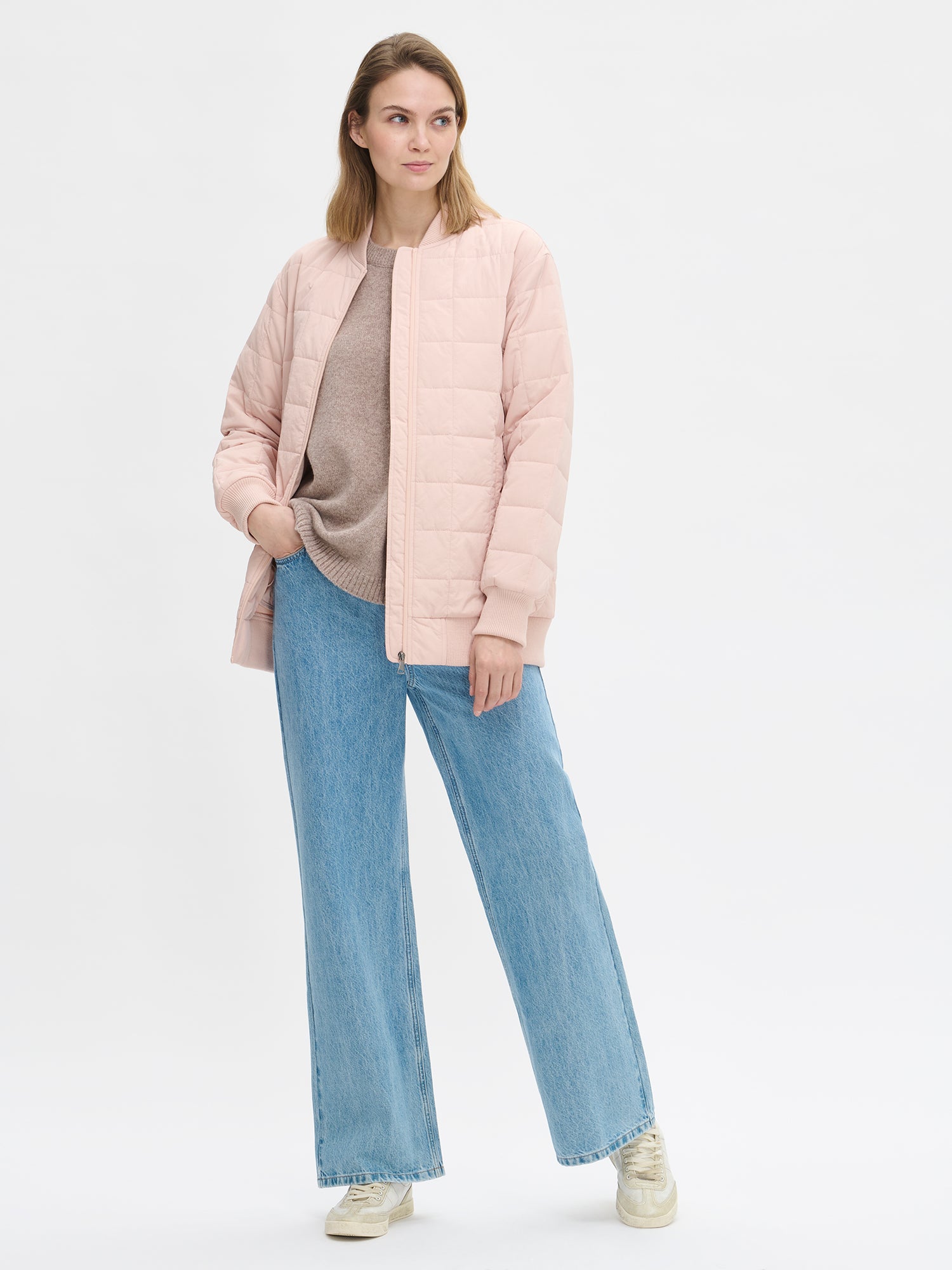 Nanso MERJE Quilted Bomber Jacket in Light Rose features a lightweight Sorona -insulation, ribbed knit detailing at the neckline, cuffs, and hem. Dropped shoulders create a relaxed, contemporary silhouette. Photographed on a model with jeans on, jacket open.