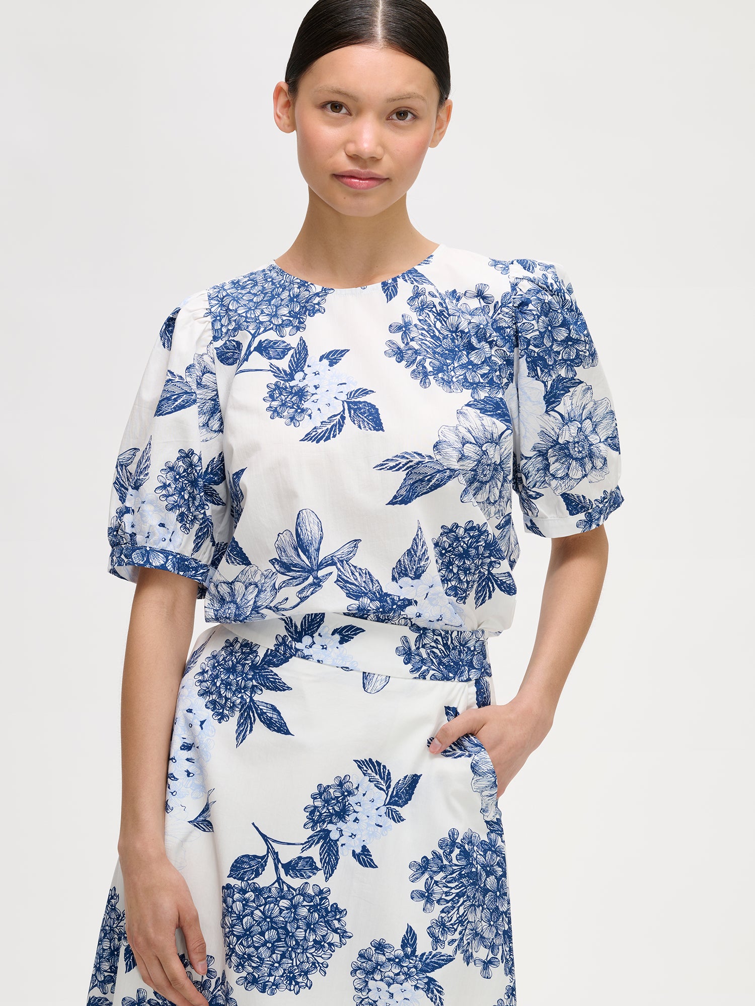 Palatsi blouse features a delicate floral pattern in blue and white, pictured on a model with a matching skirt, close-up.