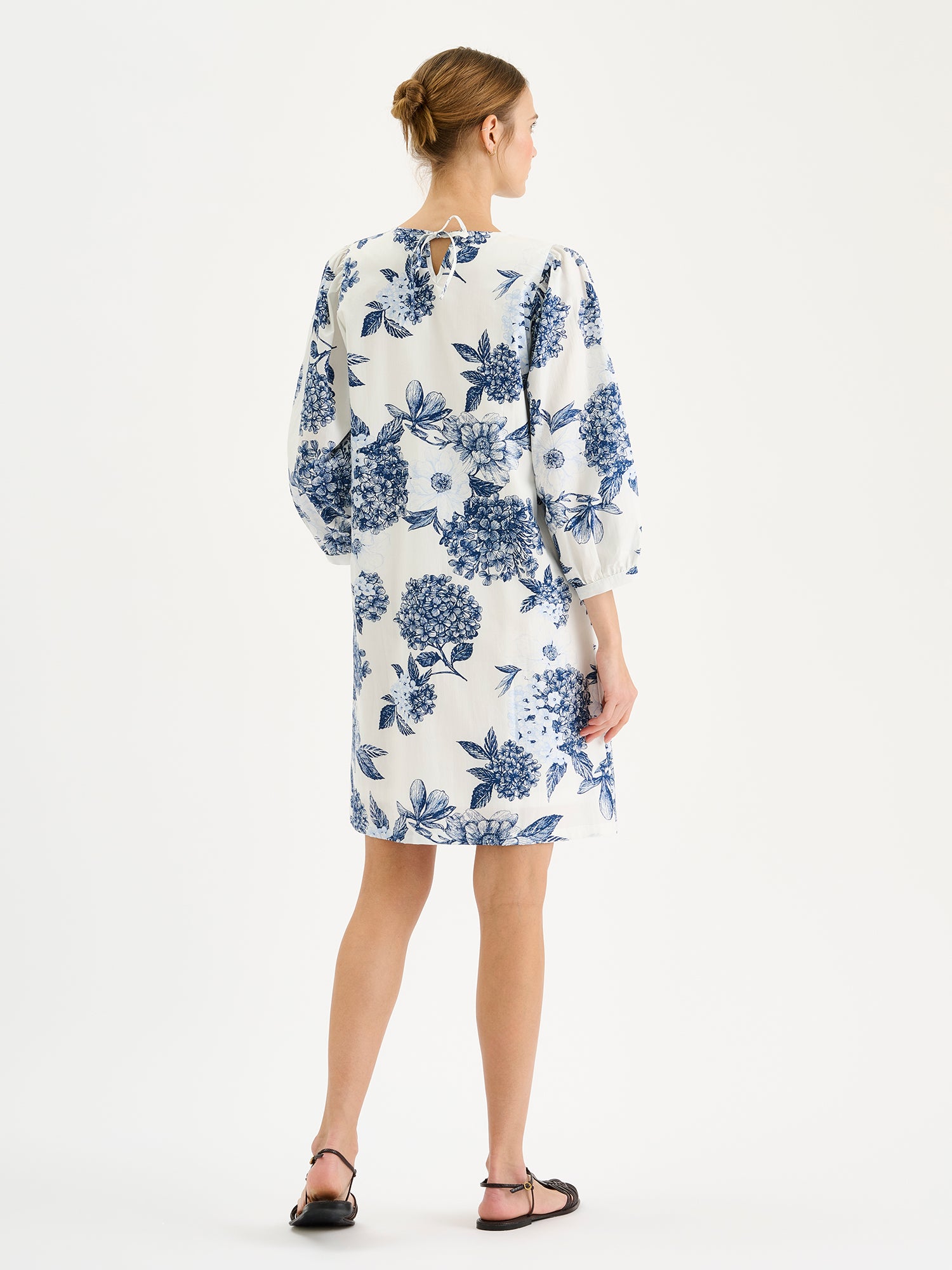Nanso Palatsi Dress in a striking blue and white floral pattern on a model with sandals, pictured from the backside.
