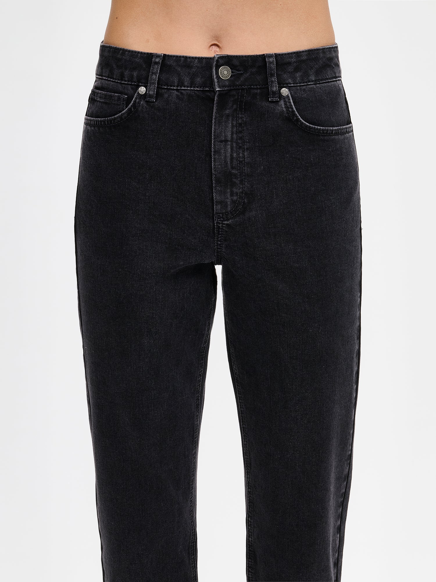 Nanso Cropped Kapee jeans feature a classic mid-rise waistband with a zippered fly and button closure for a secure fit. Practical front and back pockets provide convenient storage. On a model close-up from the front.