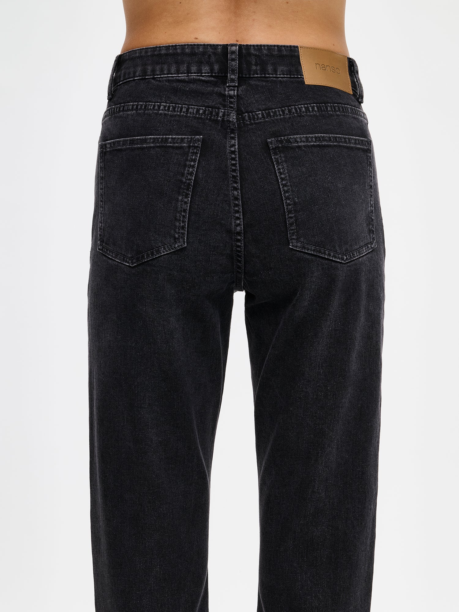 Nanso Cropped Kapee jeans feature a classic mid-rise waistband with a zippered fly and button closure for a secure fit. Practical front and back pockets provide convenient storage. On a model close-up-from the back.