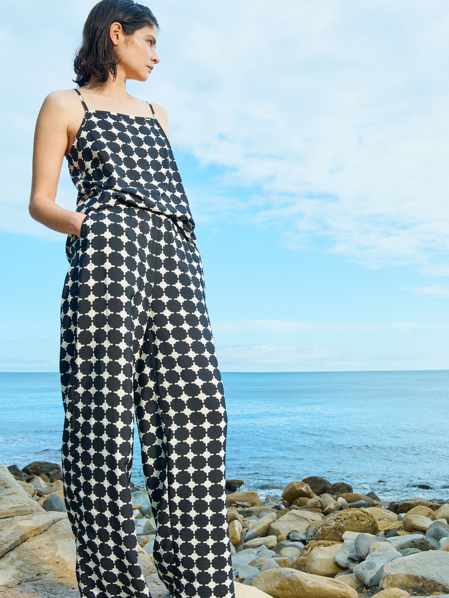 Nanso women's patterned black and white Avene woven top with adjustable spaghetti straps, on a model with matching trousers pictured on a beach scenery.
