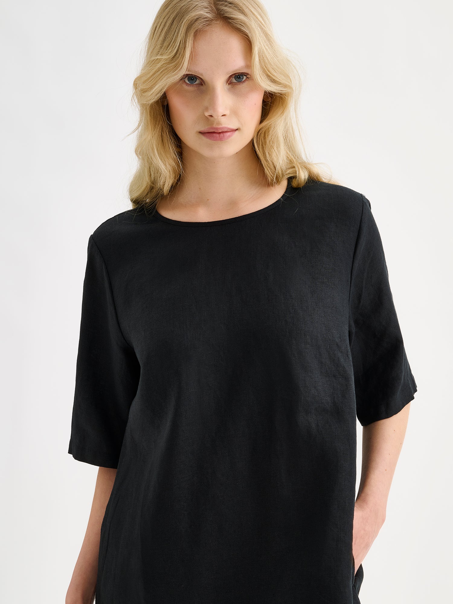 Nanso women's black relaxed Liisu linen dress with half-length sleeves features a generously ruffled hem, on a model, close-up.