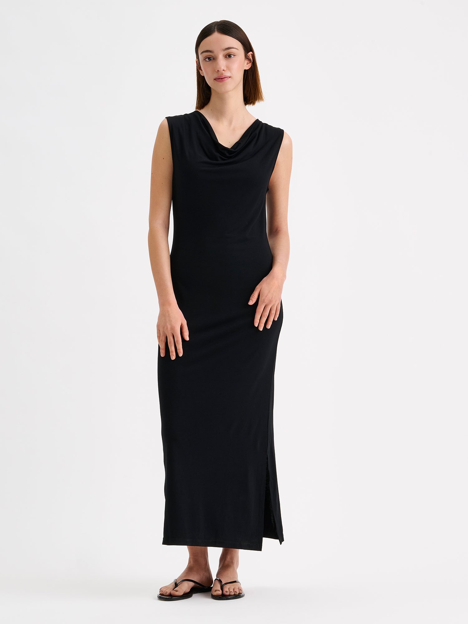 Nanso women's timeless Vivian black dress combines effortless style and comfort. This sleeveless maxi dress features an elegant draped neckline and a subtle side slit. Pictured on a brunette model.