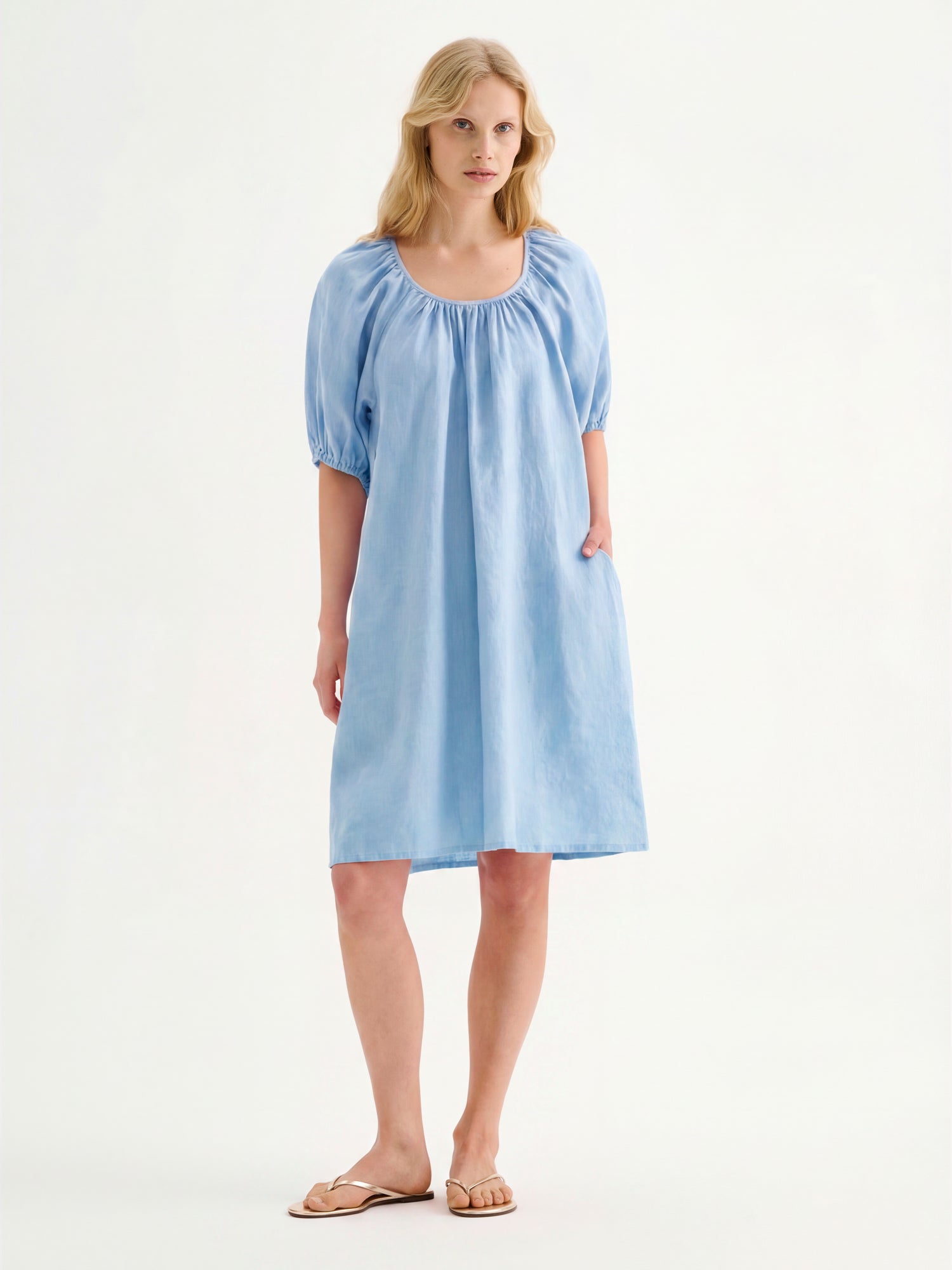 Nanso women’s beautifully relaxed light blue Donna linen dress. This airy short dress features a softly gathered open back neckline, finished with a tie-back bow detail. Pictured on a model with sandals.