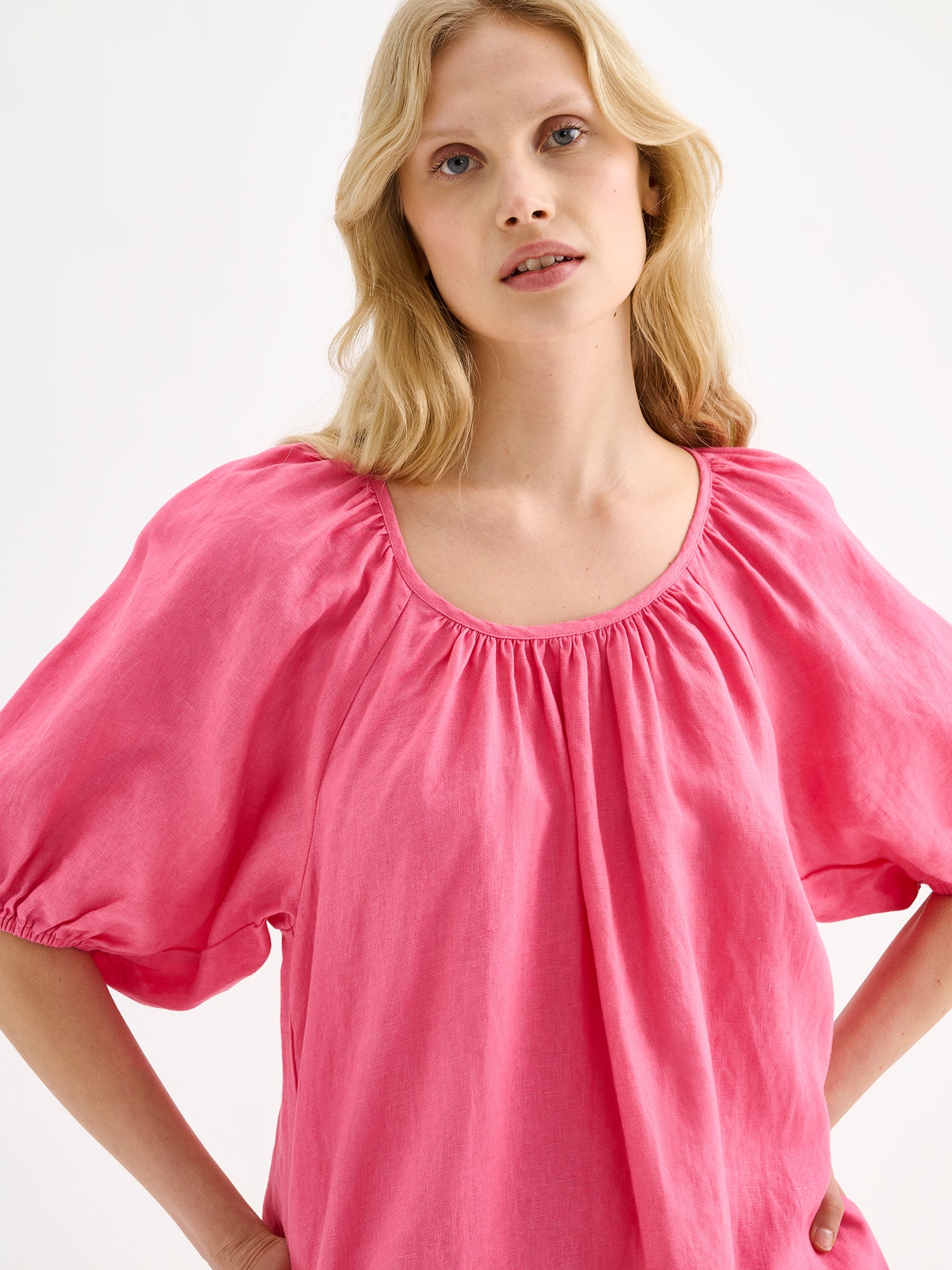 Nanso women’s beautifully relaxed pink Donna linen dress. This airy short dress features a softly gathered open back neckline, finished with a tie-back bow detail. Pictured on a model close-up.