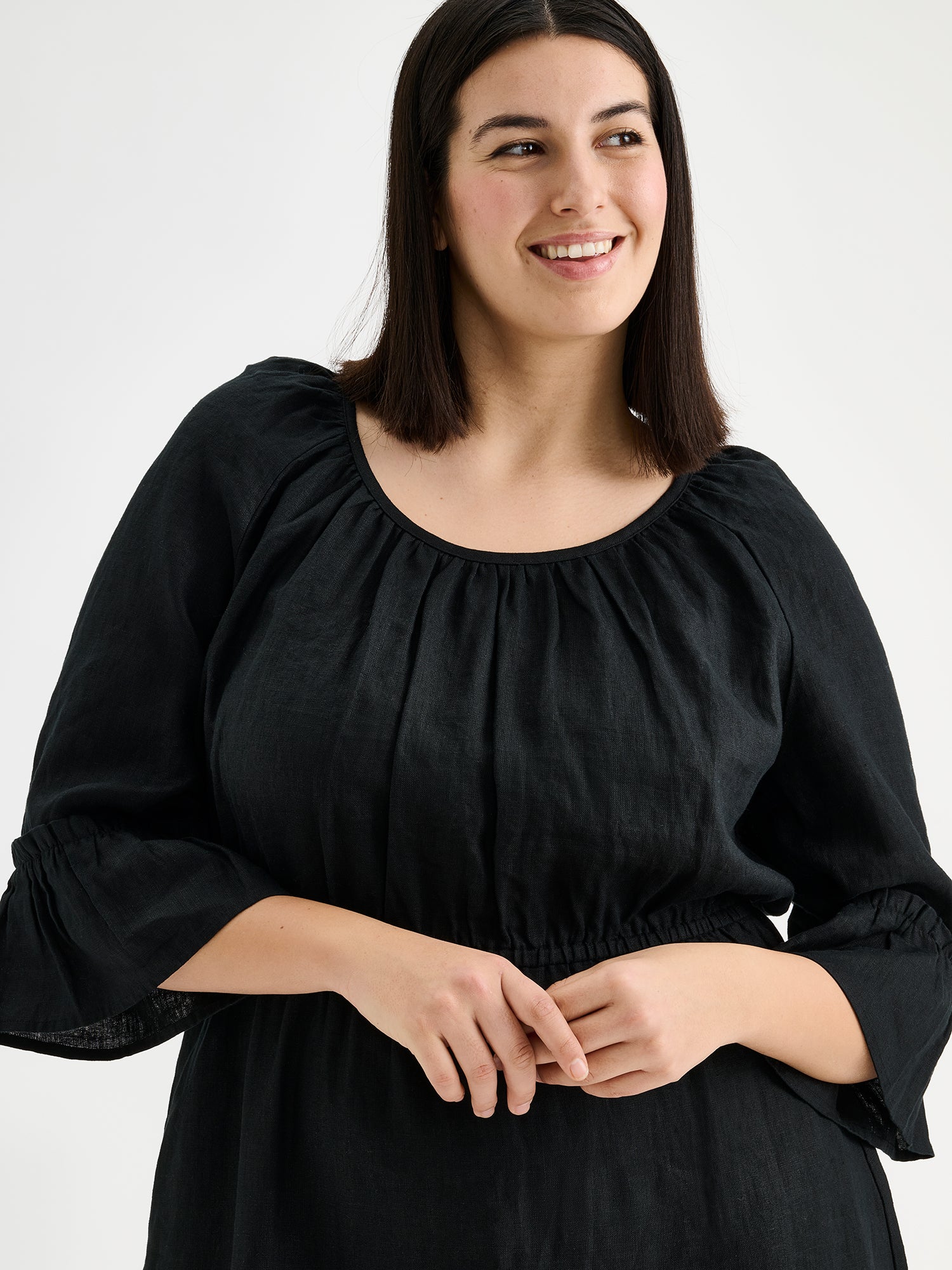 Nanso women's black Donna midi linen dress combines effortless elegance with feminine details. This airy midi-length style features an open, softly gathered back neckline with a striking self-tie bow. Pictured on a brunette model, close-up.