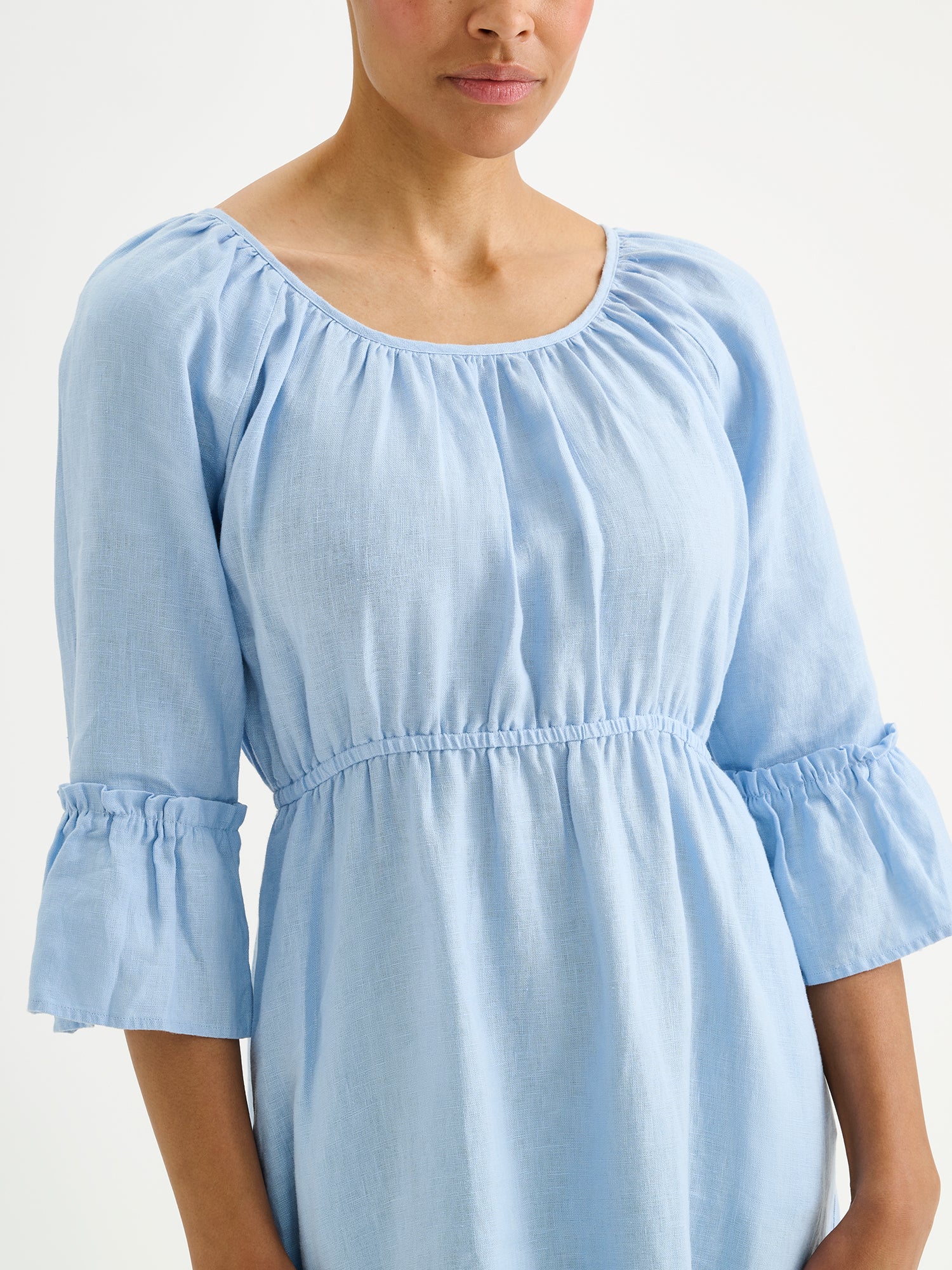 Nanso women's softly light blue Donna midi linen dress combines effortless elegance with feminine details. This airy midi-length style features an open, softly gathered back neckline with a striking self-tie bow. Pictured on a model, close-up