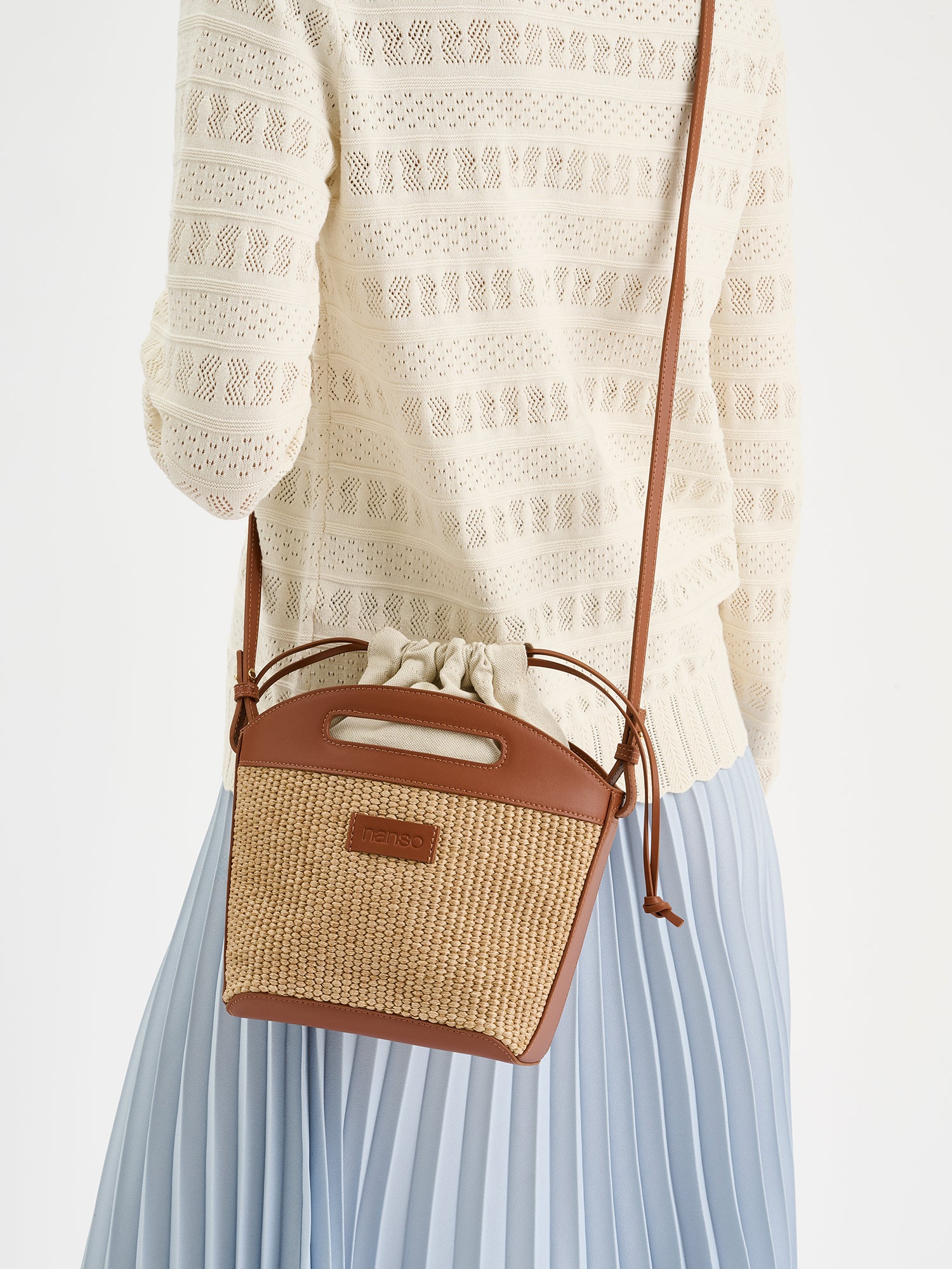 Crafted from durable straw-like material, the KORI Bag in Beige is a versatile cross body bag that is secured with elegant leather straps. The bag photographed on a model.