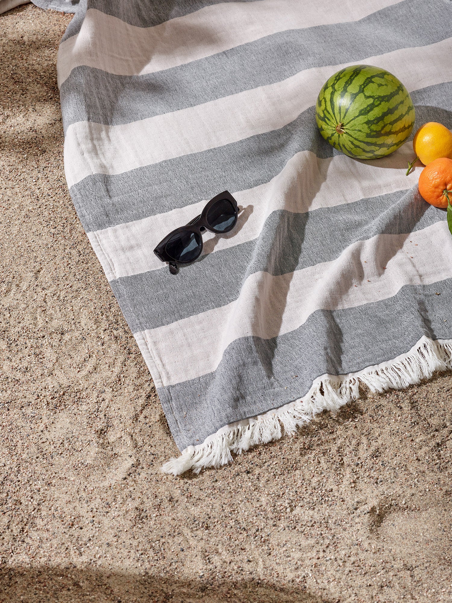lightweight Amalfi bath towel in classic black and white, pictured on a beach with sunglasses and fruits.
