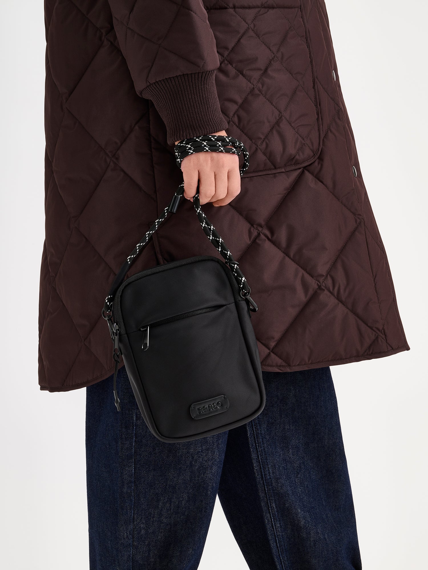 Nanso women's stylish black Tuuli crossbody bag crafted from nylon fabric, pictured in models hand, model wearing a brown quilted coat and jeans.