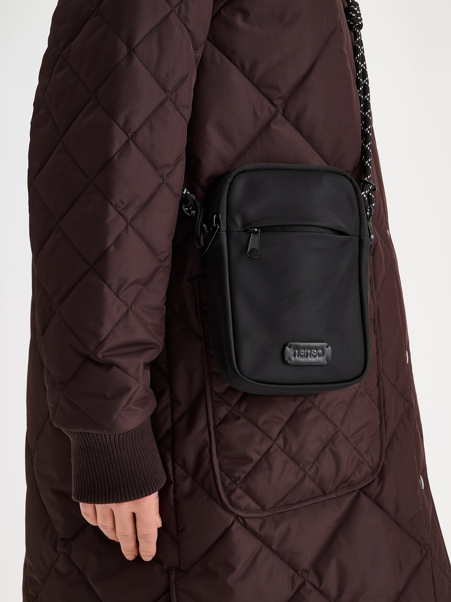 Nanso women's stylish black Tuuli crossbody bag crafted from nylon fabric, pictured in on a model wearing a brown quilted coat.