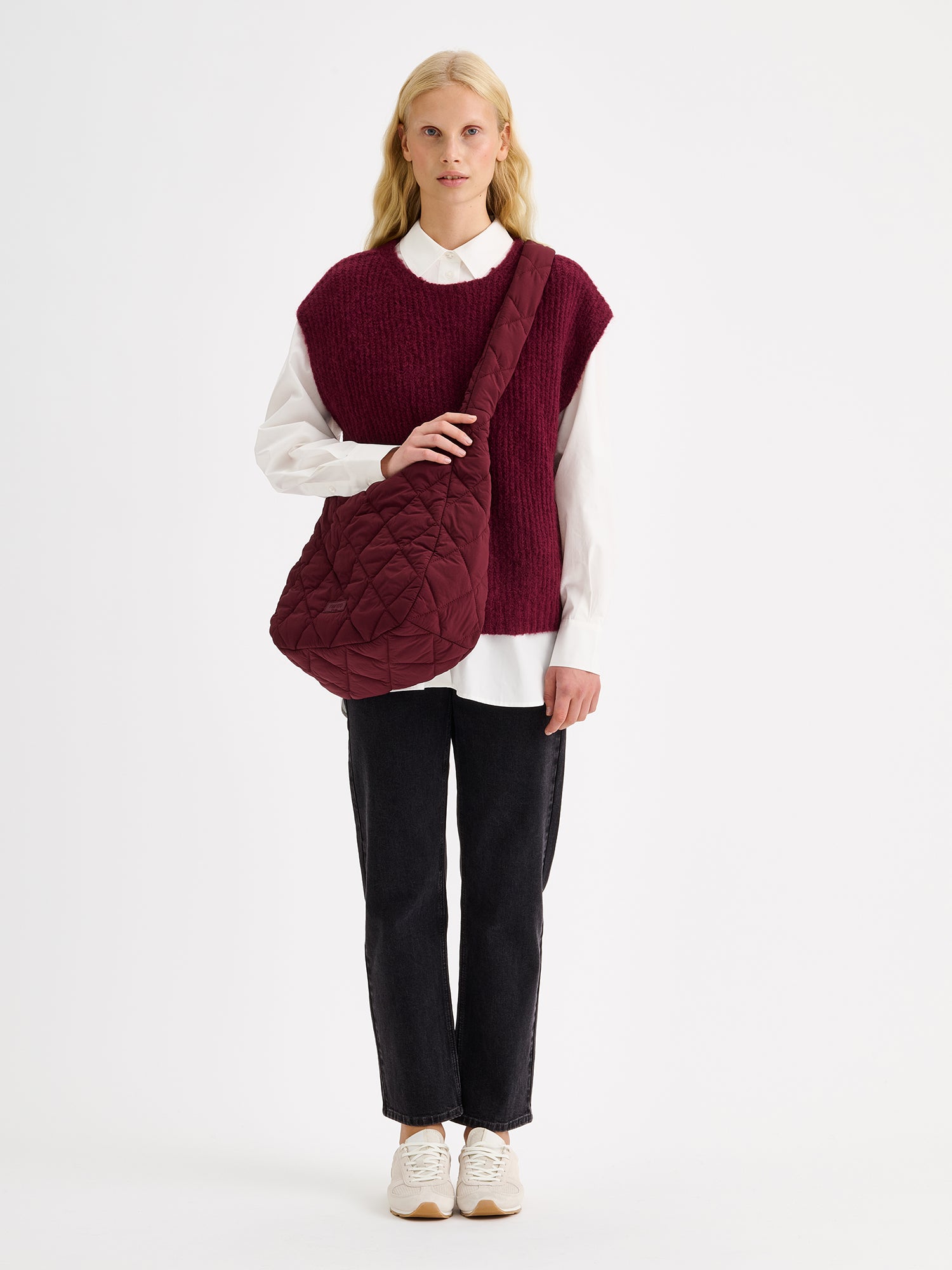 Nanso women's luxuriously soft and wonderfully chunky, the Karamelli knitted vest in a rich wine-red hue on a model with a white shirt and gray jeans
