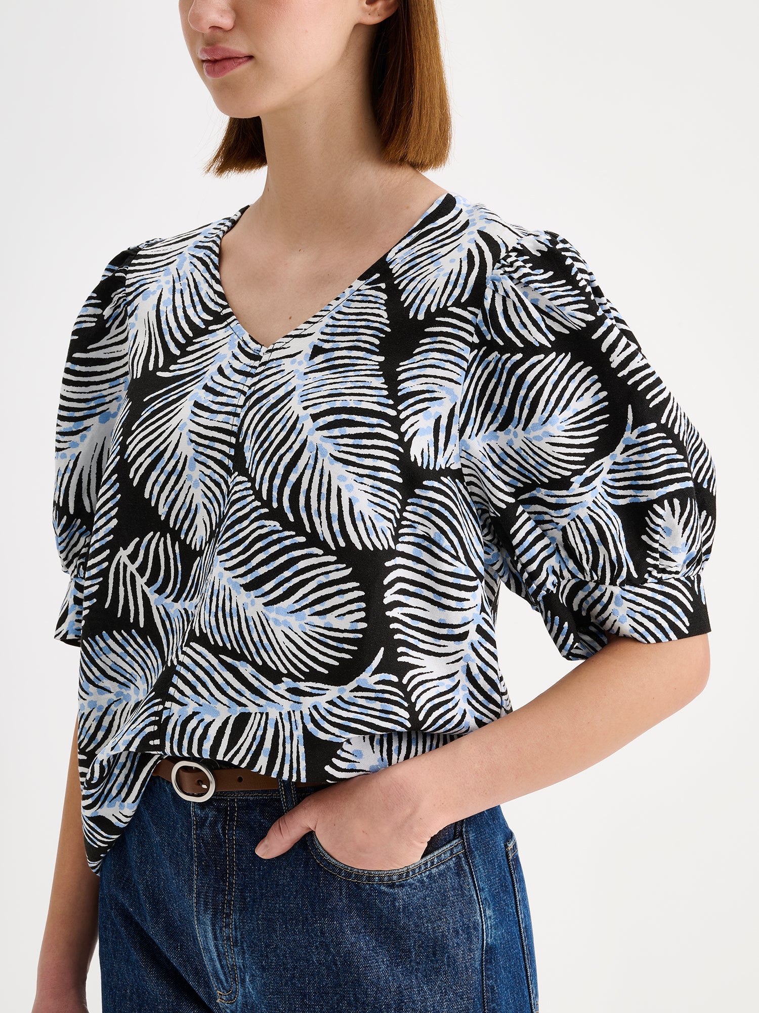 Nanso women's patterned Hilde blouse captivates with its elegant graphic and delicate pattern, flattering V-neckline and puff-sleeves. Pictured on a model with wide blue jeans, close-up.