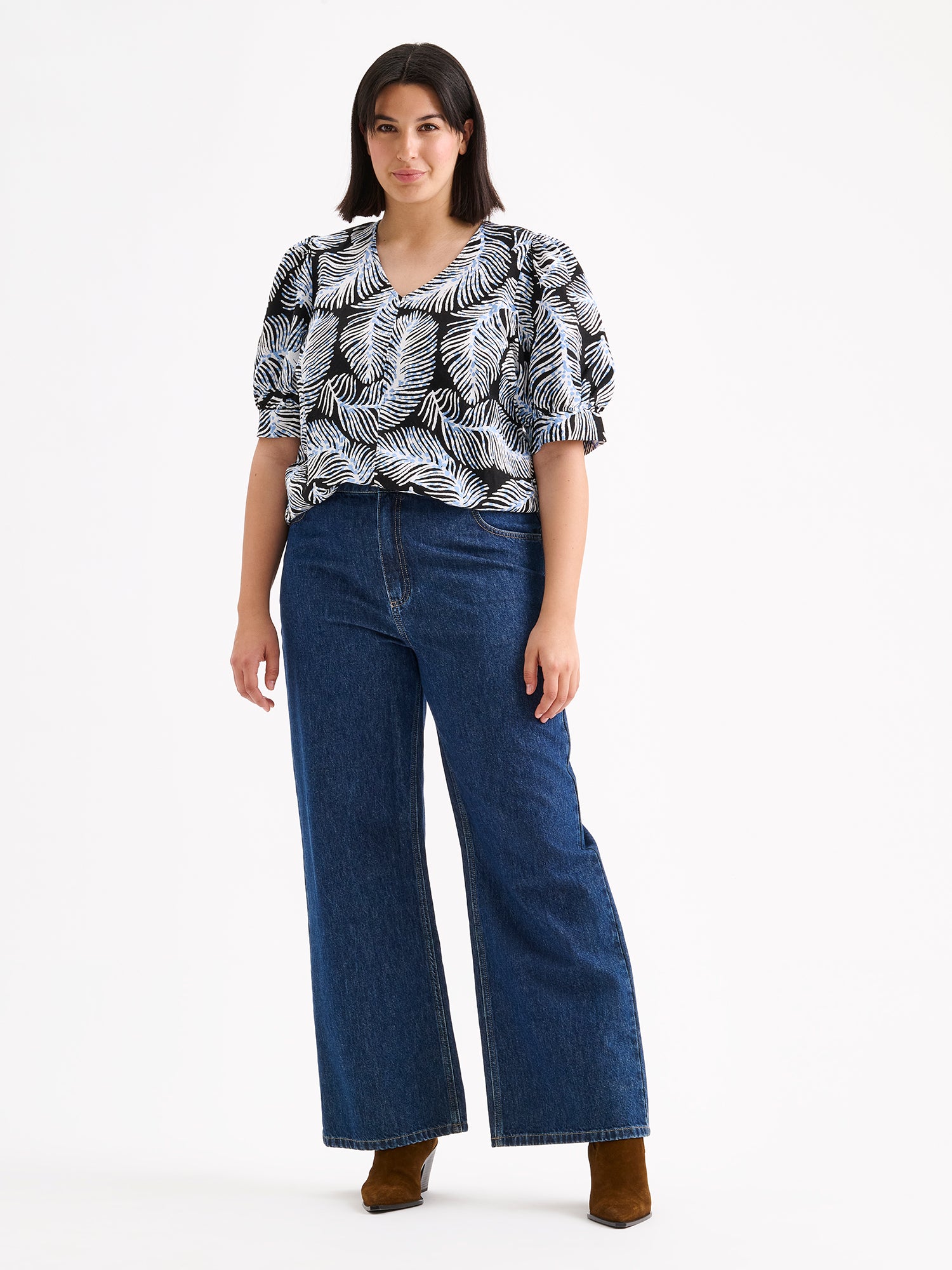 Nanso women's patterned Hilde blouse captivates with its elegant graphic and delicate pattern, flattering V-neckline and puff-sleeves. Pictured on a model with wide blue jeans.