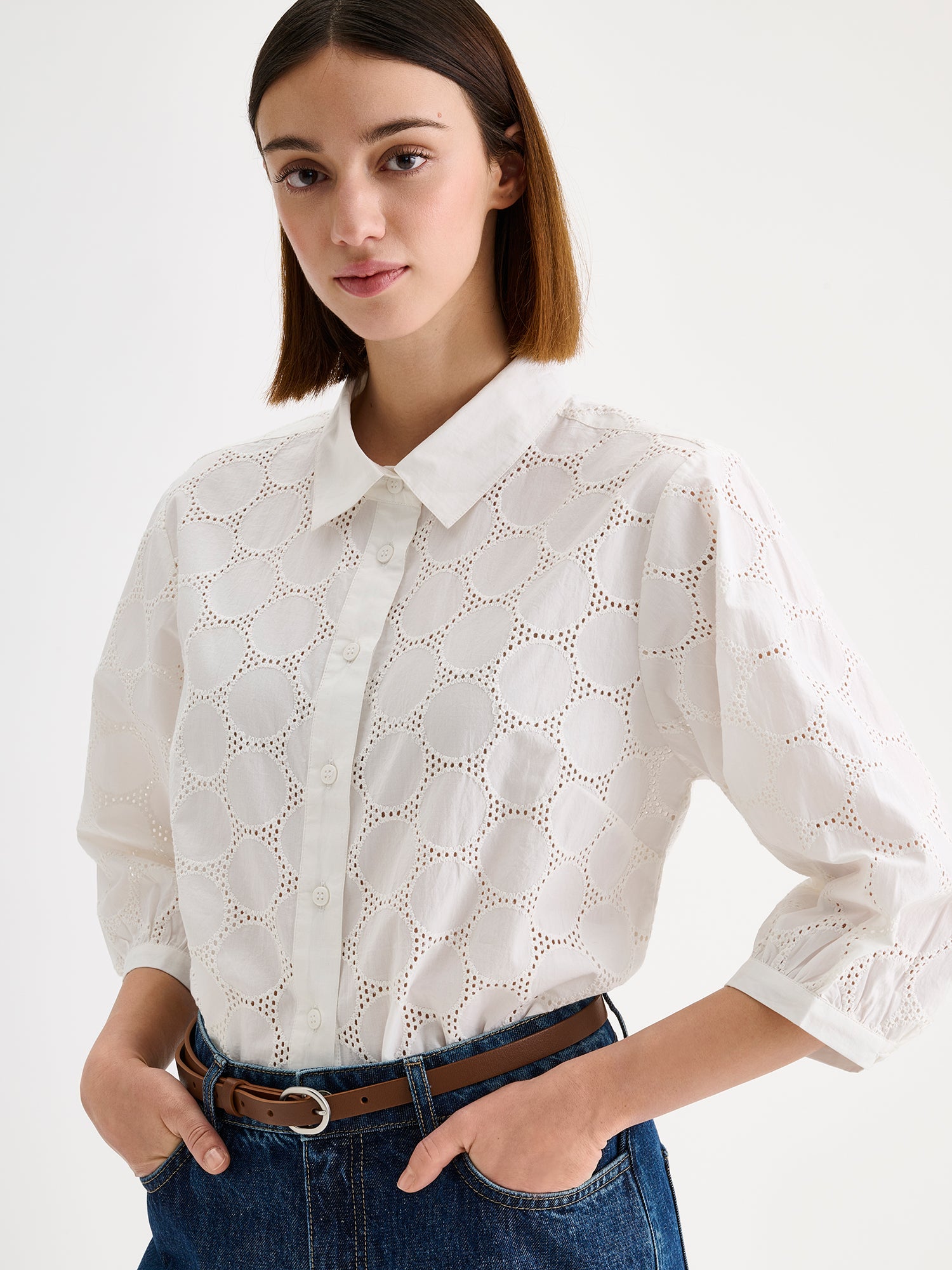 nanso women's stylish white Siiri blouse for women, featuring beautiful embroidered fabric, classic collar, buttons and 3/4 sleeves, on a model with blue jeans, close-up.