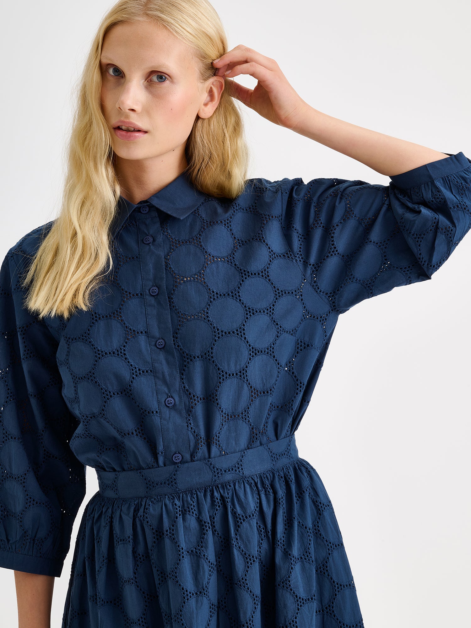 nanso women's stylish dark blue Siiri blouse for women, featuring beautiful embroidered fabric, classic collar, buttons and 3/4 sleeves, on a model with a matching skirt, close-up.