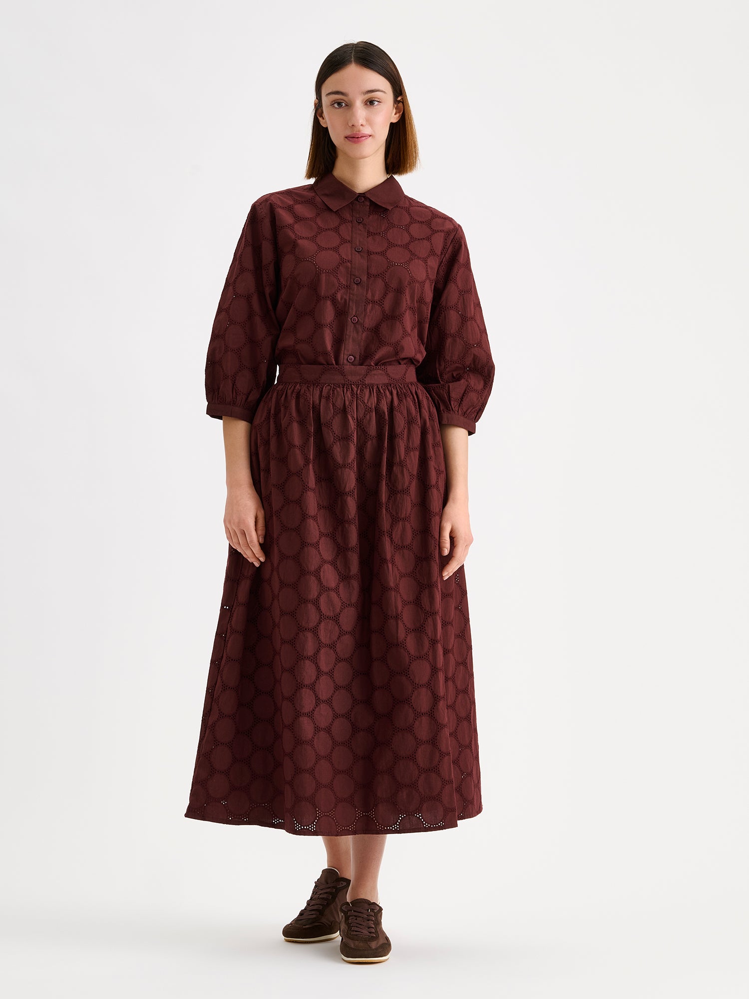 nanso women's stylish dark brown Siiri blouse for women, featuring beautiful embroidered fabric, classic collar, buttons and 3/4 sleeves, on a model with a matching skirt.