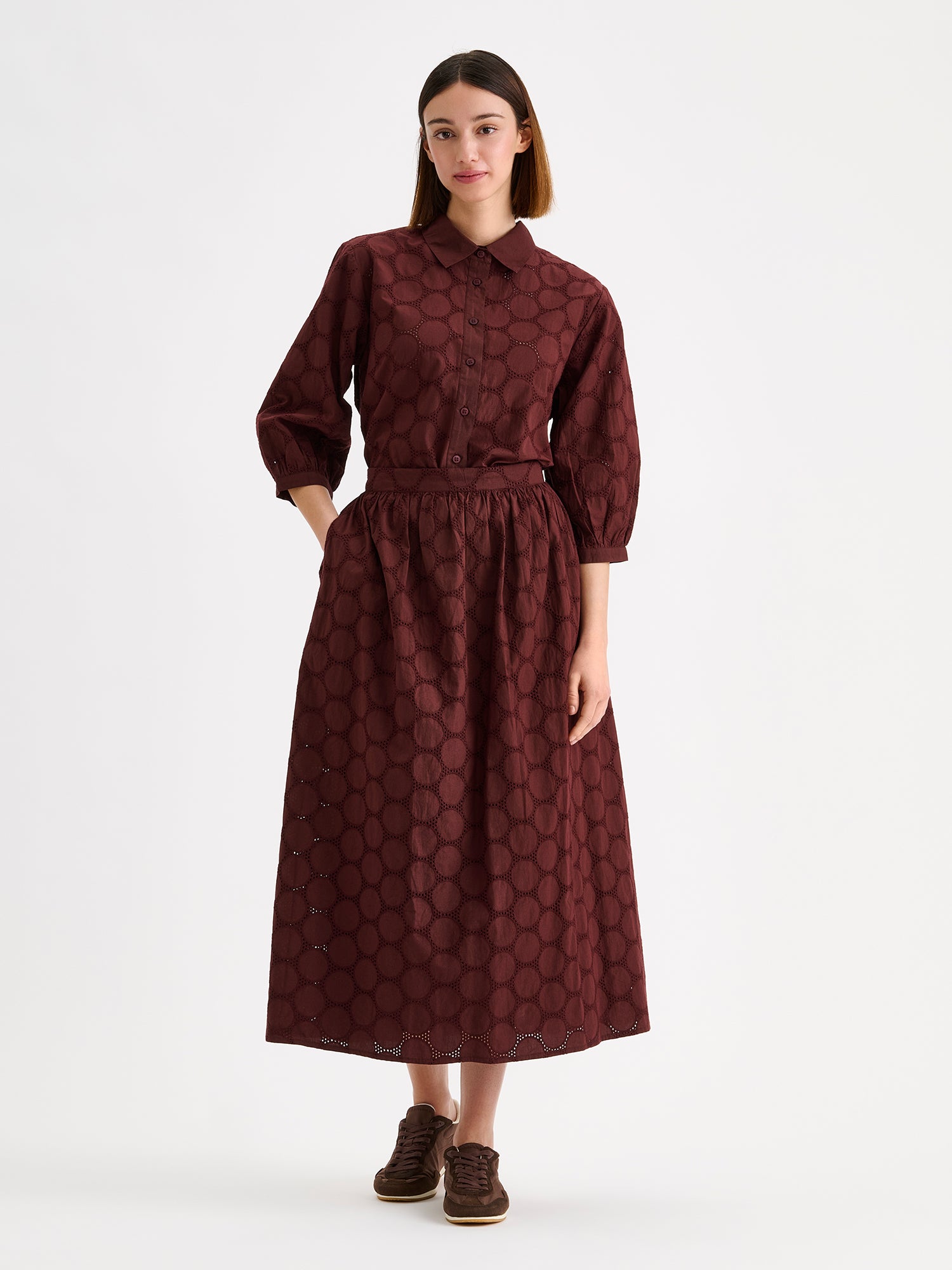 Nanso women's dark brown Siiri midi skirt, featuring a delicate lace-like woven cotton fabric with beautiful texture, pockets and a zip, on a model with a matching blouse.