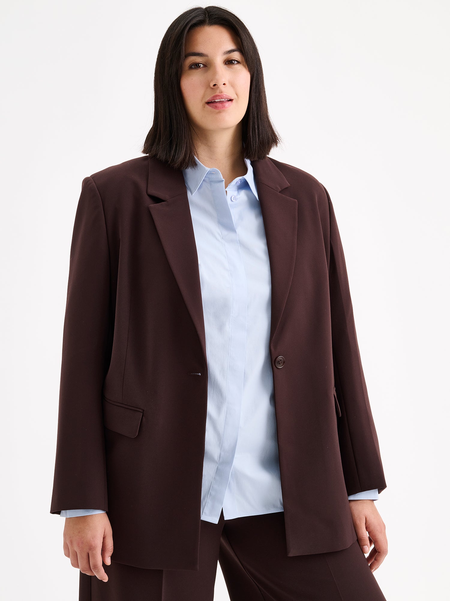 A stylish women's Eeva blazer in a rich brown shade with a relaxed yet structured silhouette, on a model with a light blue shirt