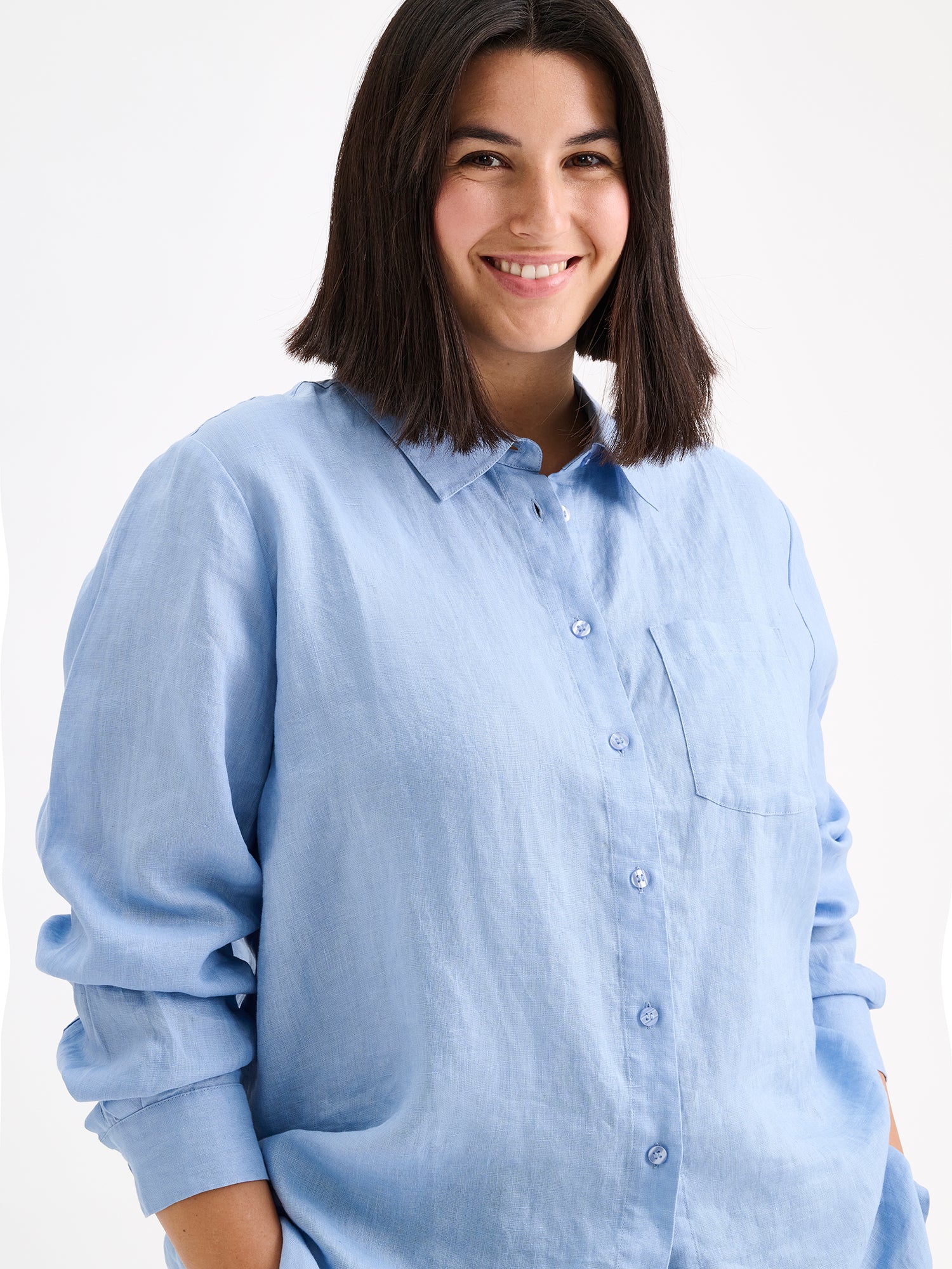 Nanso women's relaxed, classic and versatile light blue Lene linen shirt is crafted from woven linen fabric that is durable and breathable. The shirt features a front button closure and chest pocket and full-length sleeves. Pictured on a model, closeup.