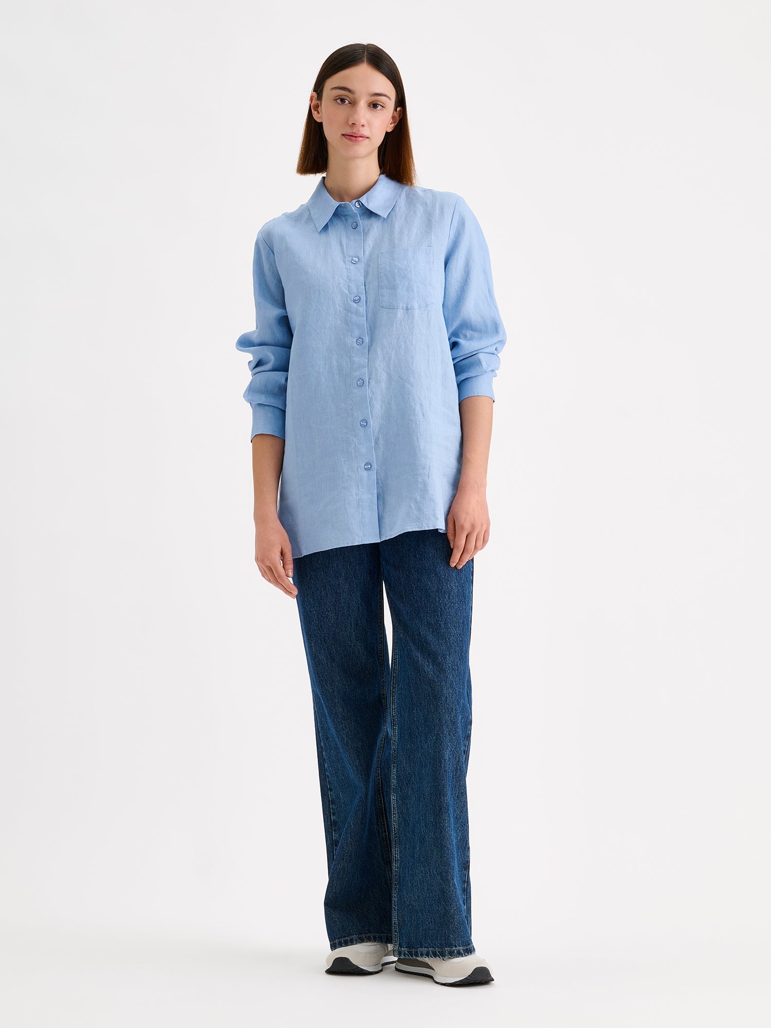 Nanso women's relaxed, classic and versatile light blue Lene linen shirt is crafted from woven linen fabric that is durable and breathable. The shirt features a front button closure and chest pocket and full-length sleeves. Pictured on a model
