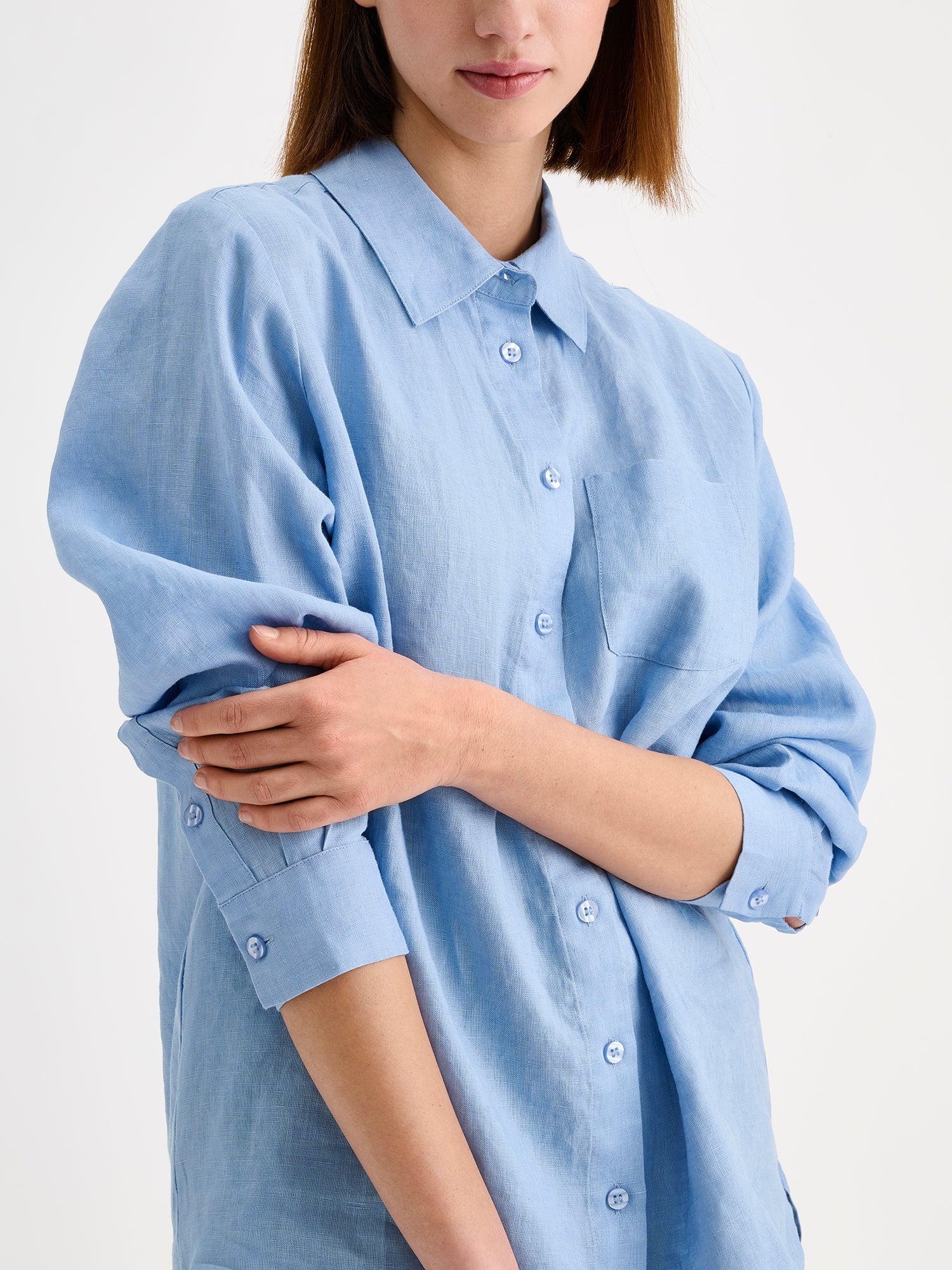 Nanso women's relaxed, classic and versatile light blue Lene linen shirt is crafted from woven linen fabric that is durable and breathable. The shirt features a front button closure and chest pocket and full-length sleeves. Pictured on a model, close up