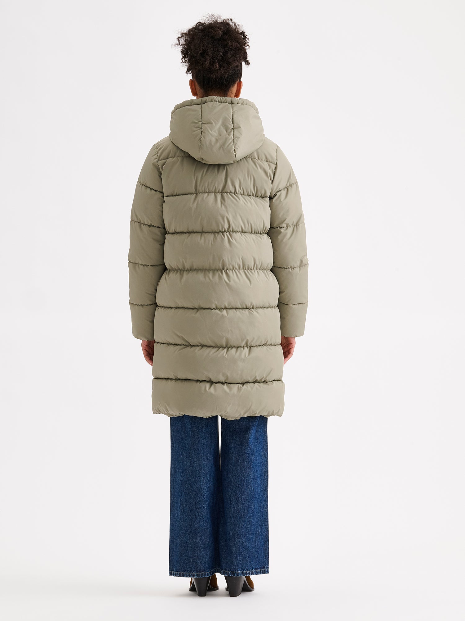 Nanso women's warm, padded yet pleasantly lightweight Lumi midi puffer coat on a model with jeans, pictured from the backside
