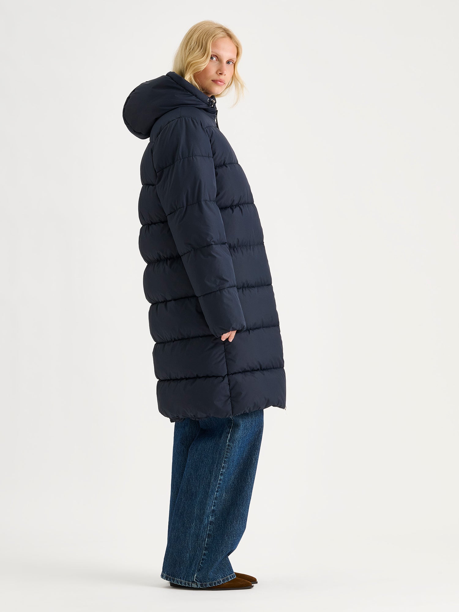 Nanso women's warm, padded yet pleasantly lightweight Lumi midi puffer coat in dark blue on a model pictured from the side