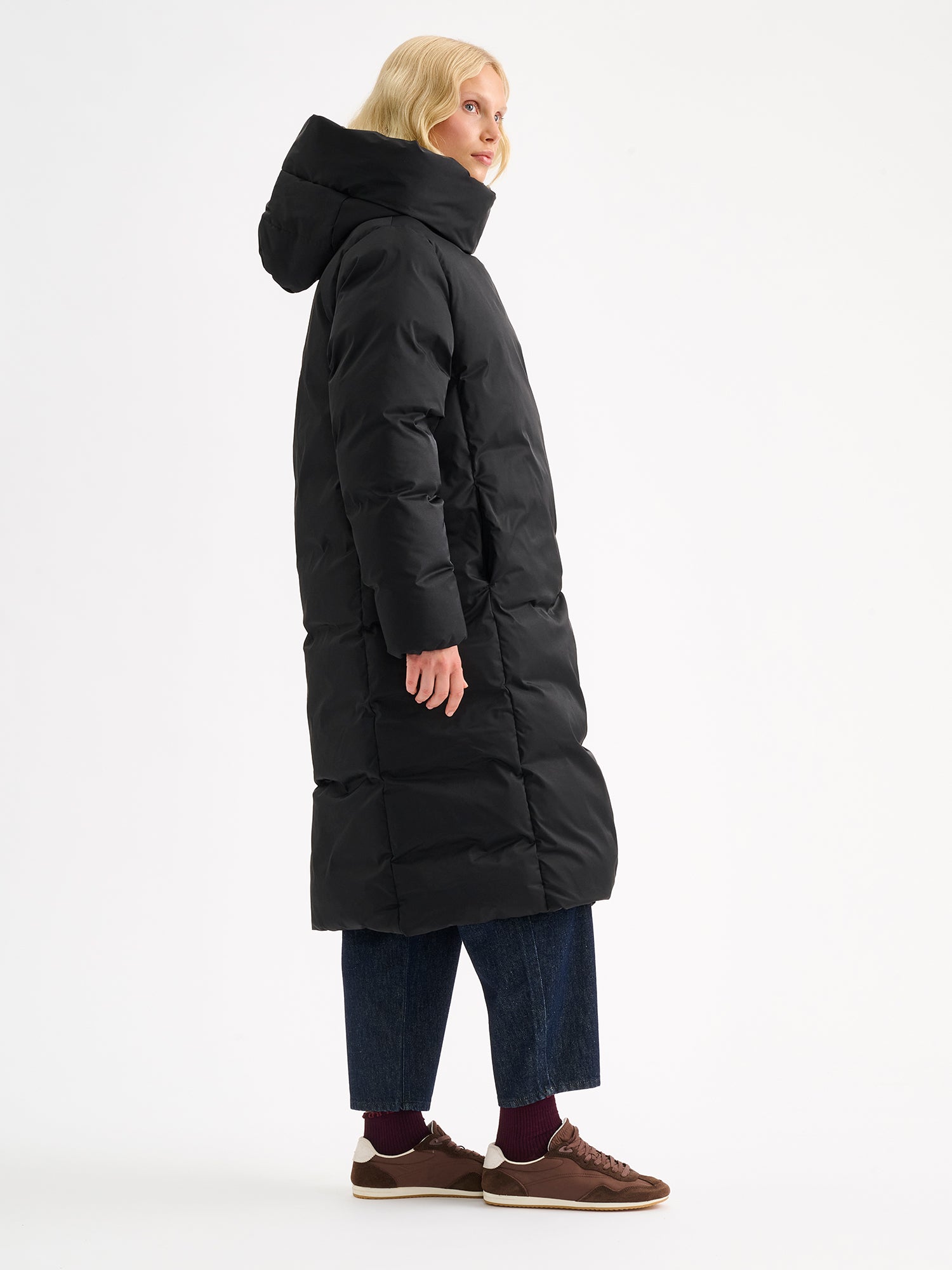 Warm and wonderfully voluminous, the long Inari puffer coat in black on a model, pictured from the side.