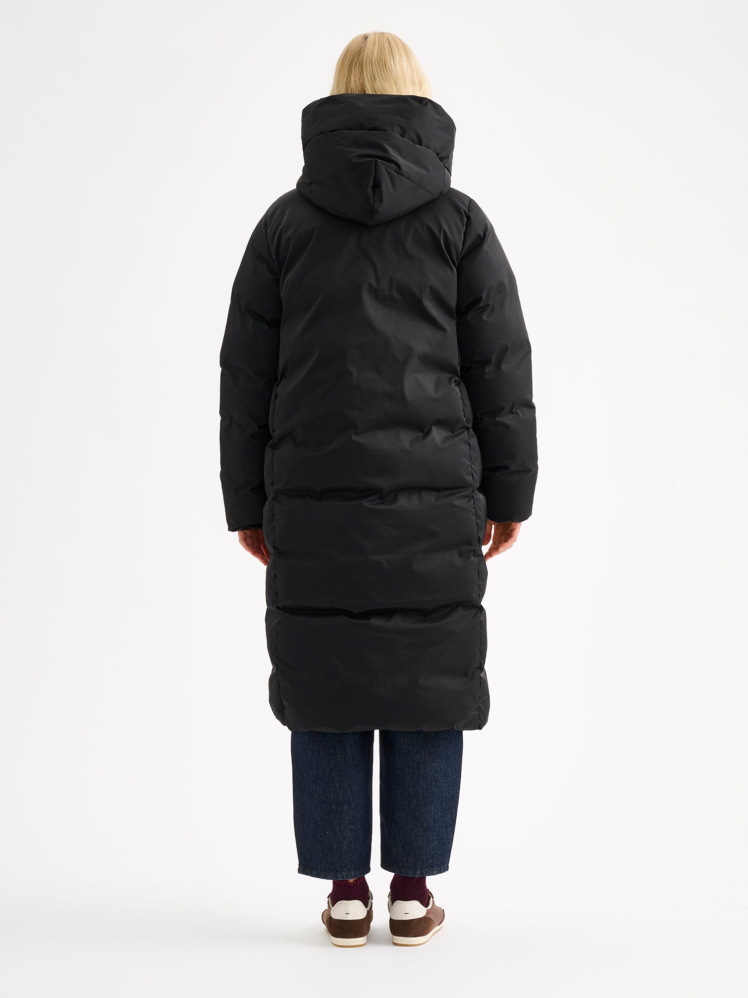 Warm and wonderfully voluminous, the long Inari puffer coat in black on a model, pictured from the backside