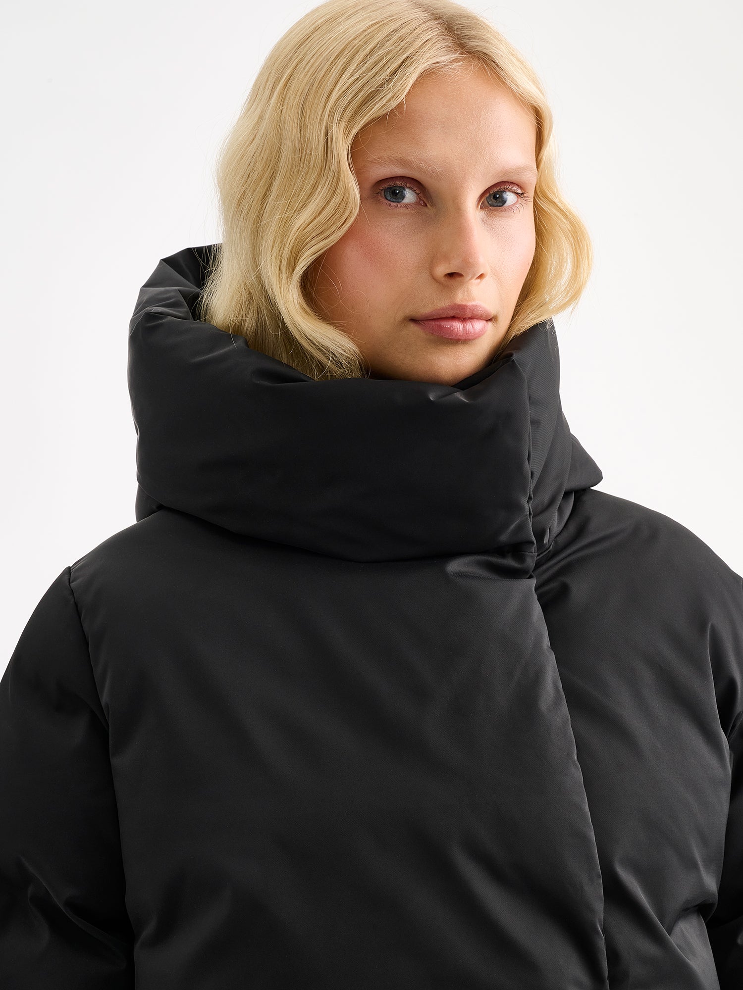 Warm and wonderfully voluminous, the long Inari puffer coat in black on a model, close-up