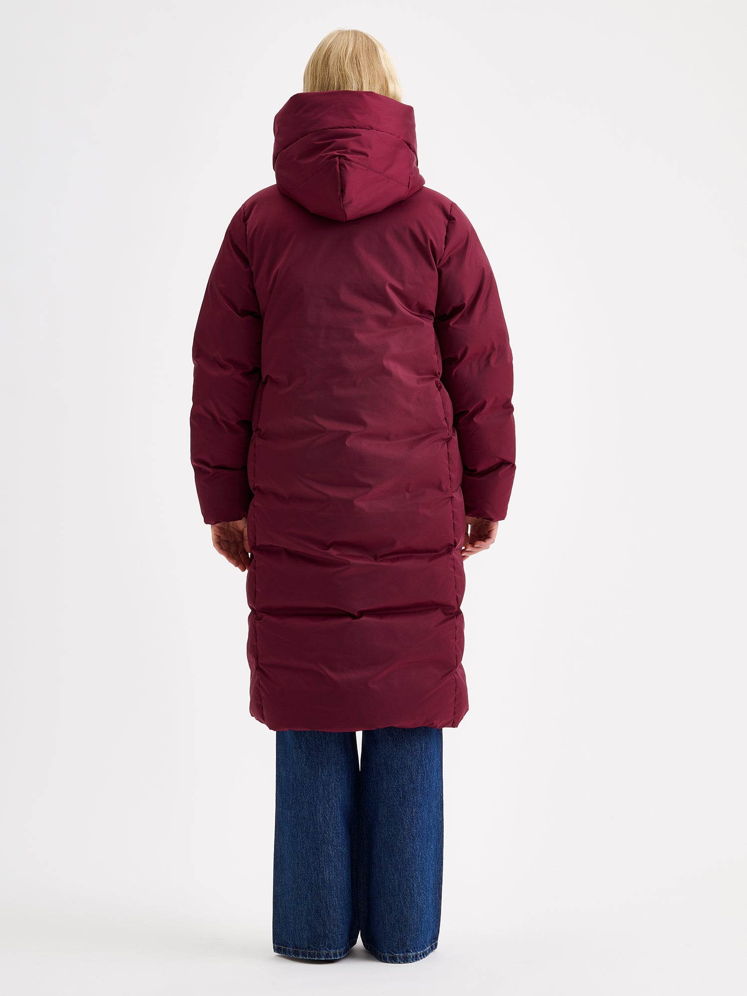 Warm and wonderfully voluminous, the long Inari puffer coat in winered on a model with jeans, pictured from the backside
