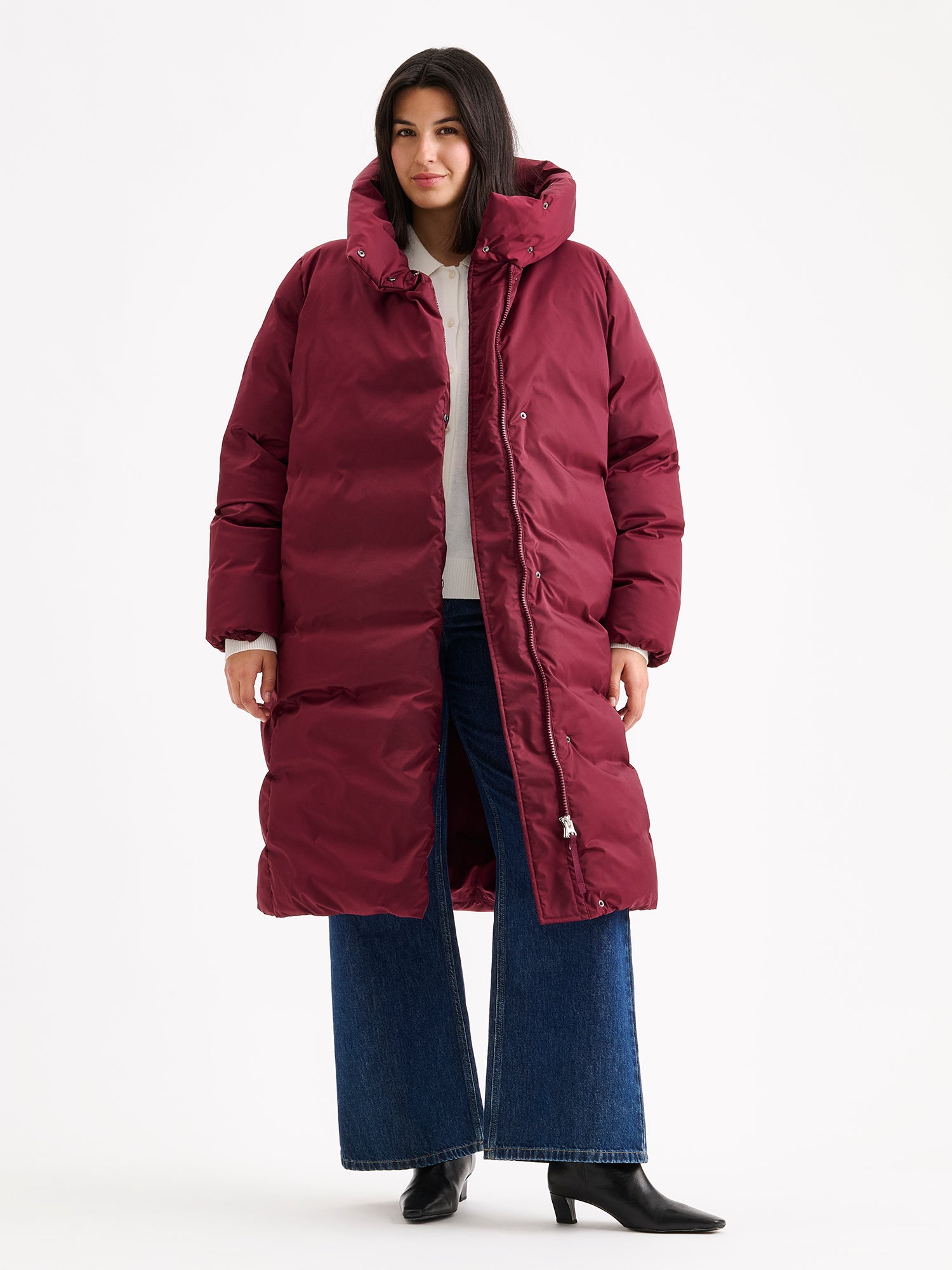Warm and wonderfully voluminous, the long Inari puffer coat in winered on a model with jeans.