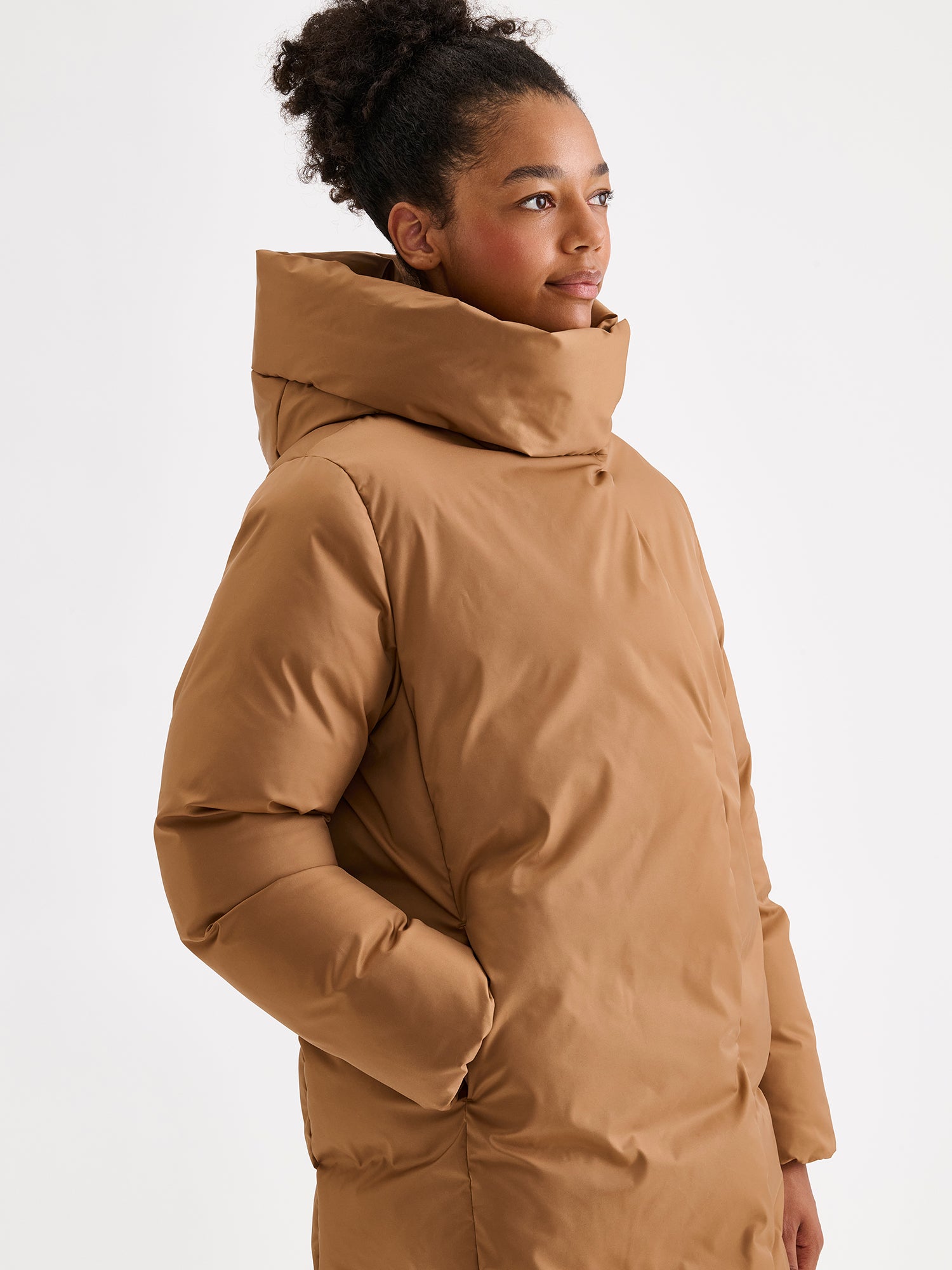 Warm and wonderfully voluminous, the long Inari puffer coat in brown. On a model close-up.
