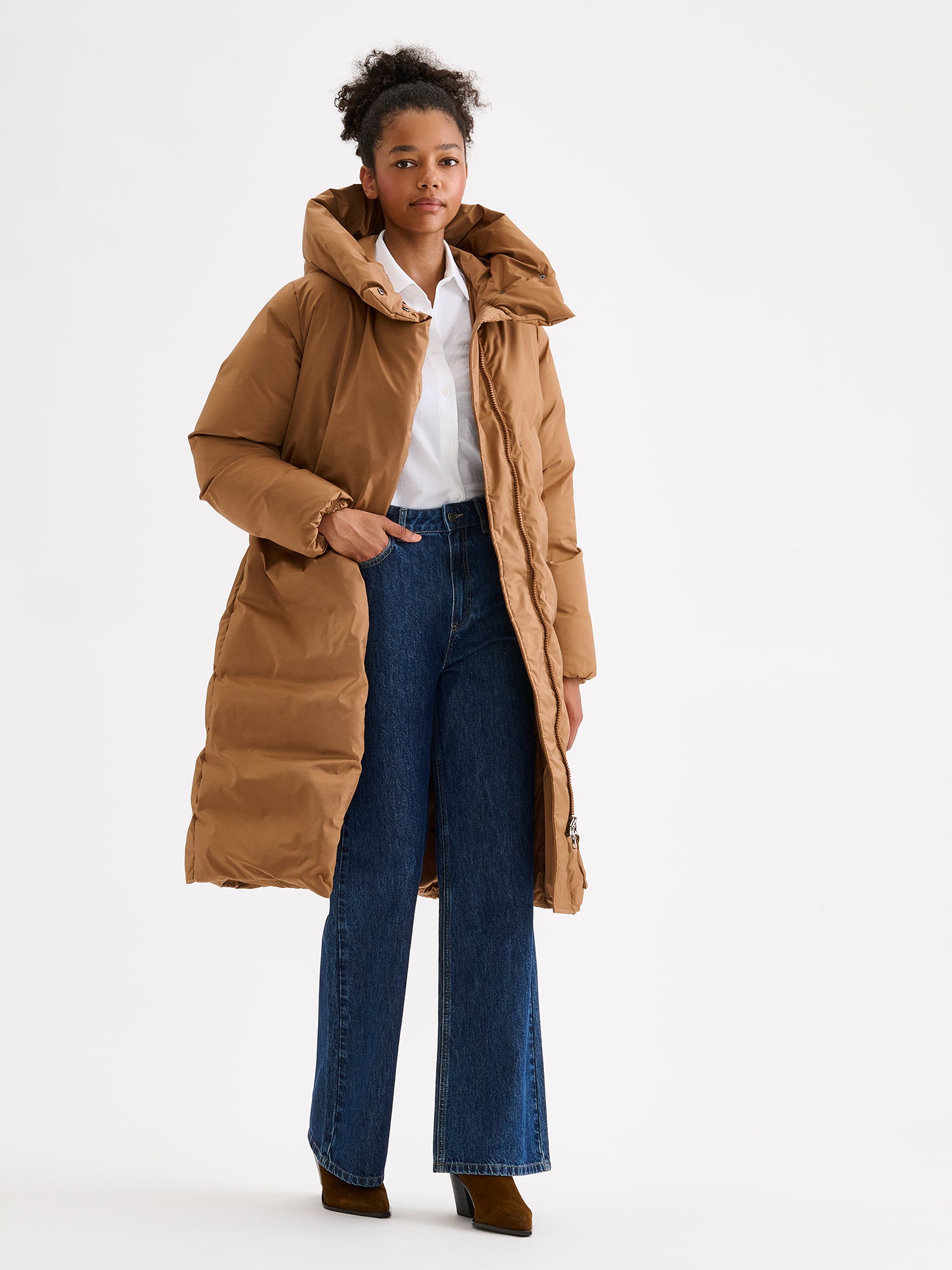 Warm and wonderfully voluminous, the long Inari puffer coat in brown. On a model with jeans