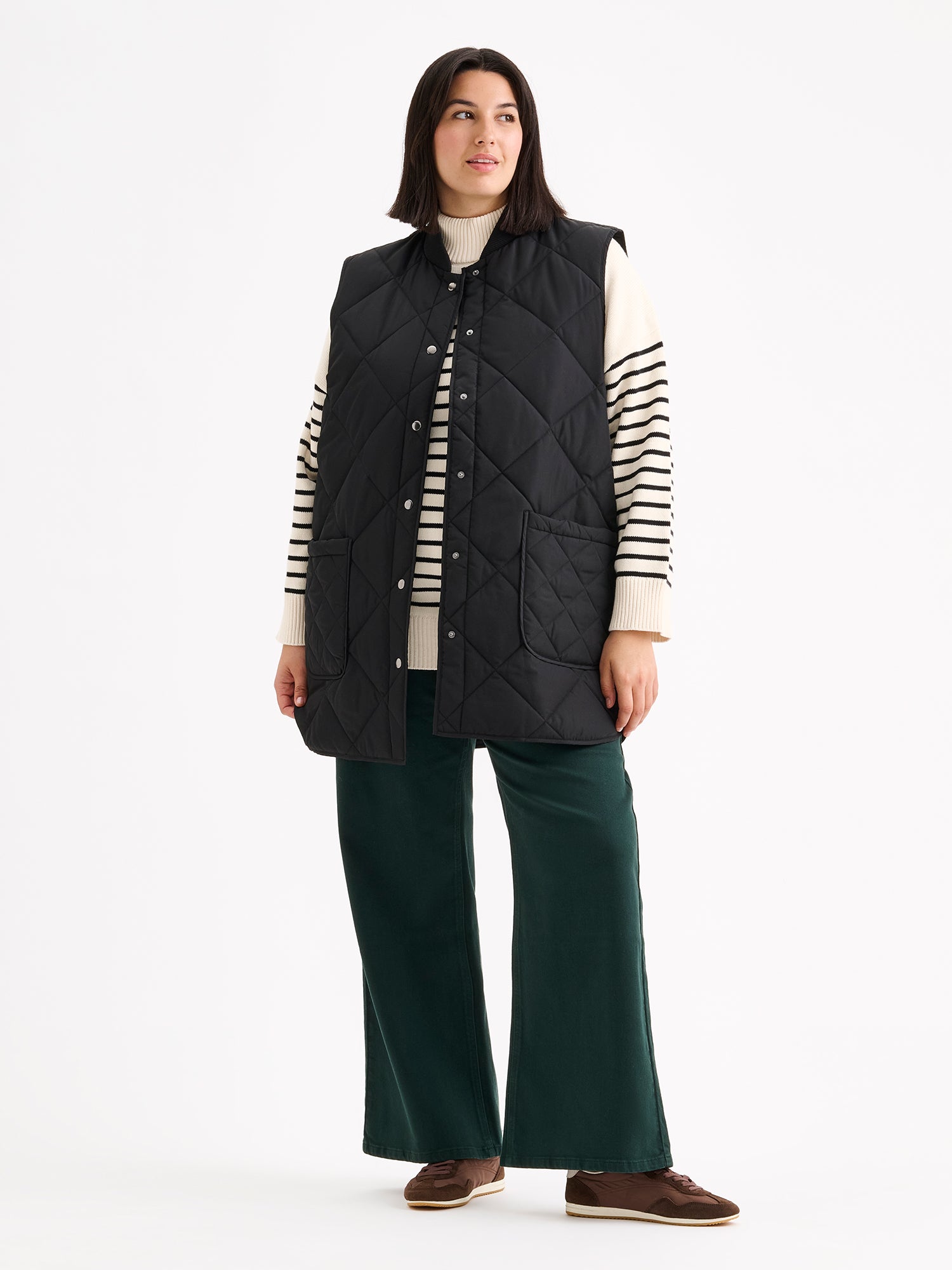 Nanso women's beautiful classic quilted vest in black, on a model with a striped sweater and wide blue jeans.