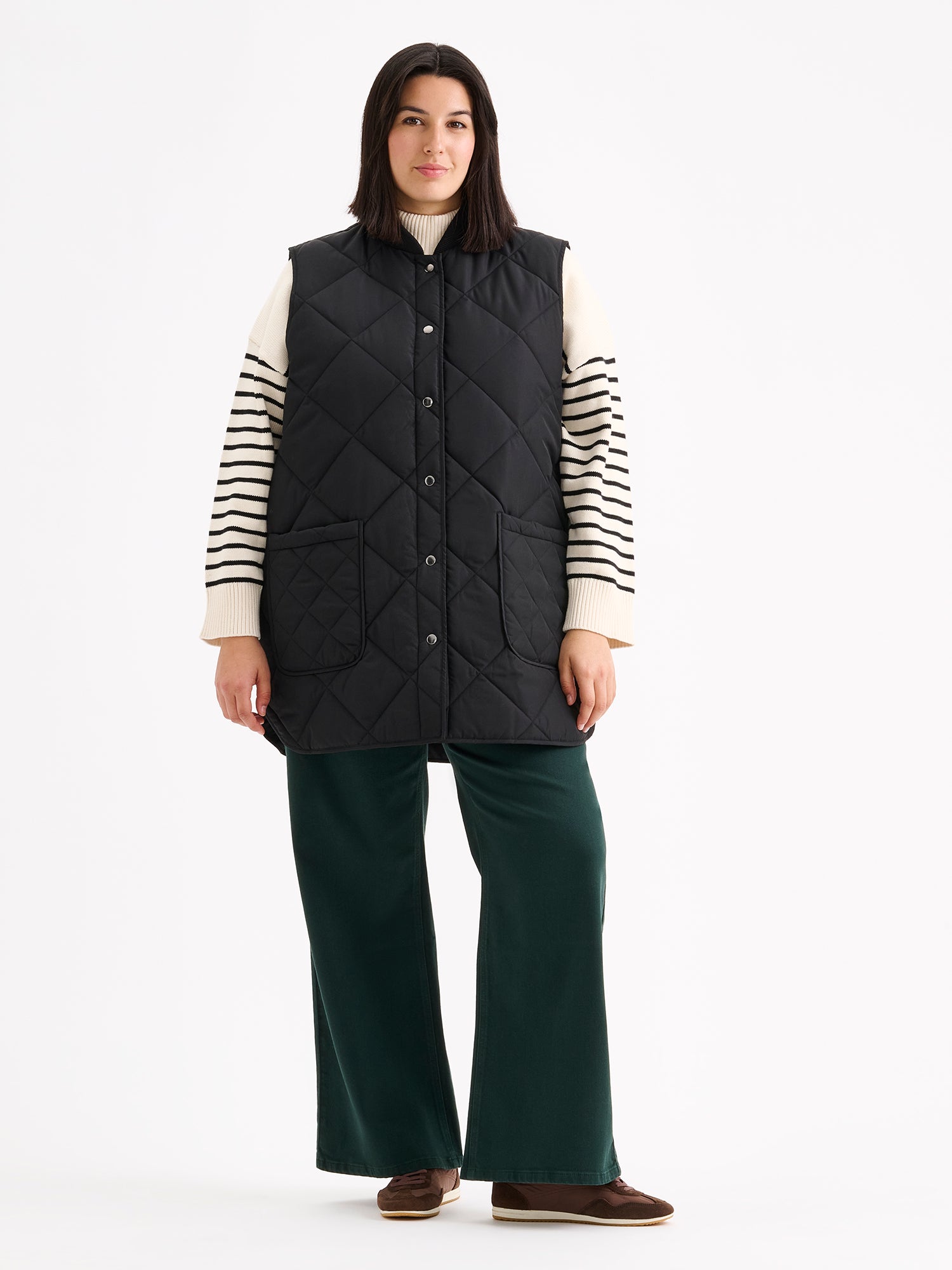 Nanso women's beautiful classic quilted vest in black, on a model with a striped sweater and wide blue jeans.