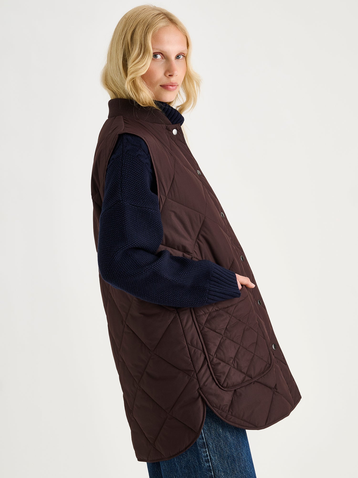 Nanso women's beautiful classic quilted vest in dark brown on a blonde model with a sweater and blue jeans.