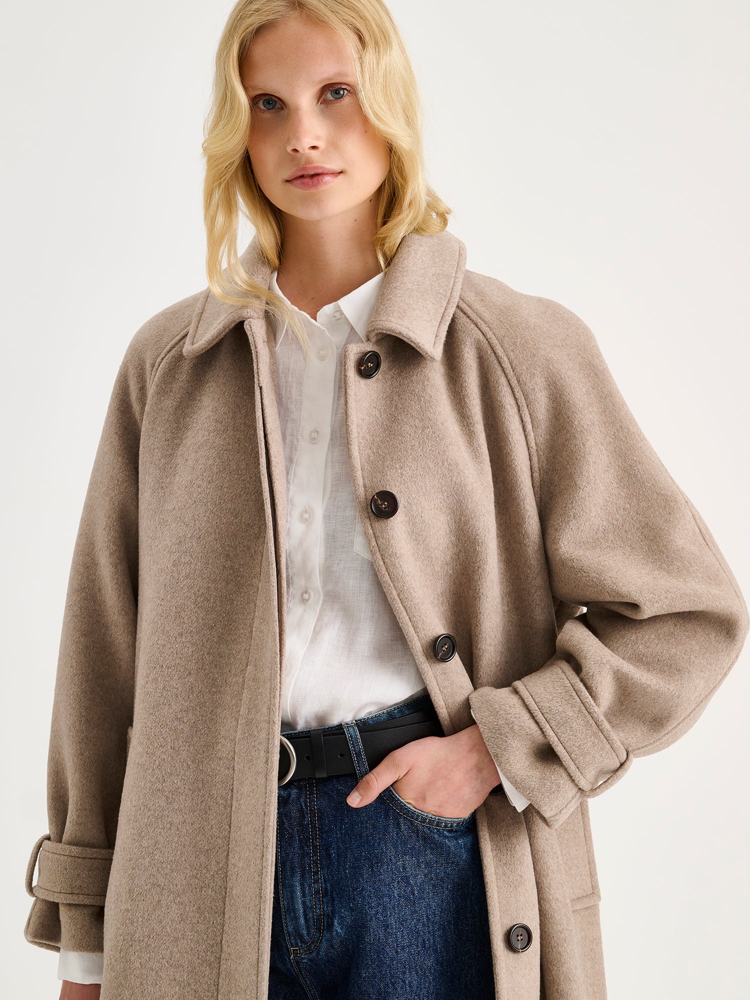 Nanso women's timelessly elegant and effortlessly classic, the Tove long wool coat in beige, on a model with blue jeans, close-up