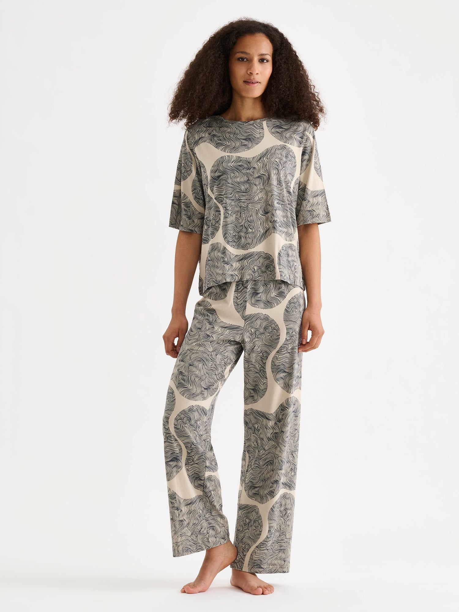 The straight-cut Paasi T-shirt for women, featuring a harmonious all-over print, is perfect for relaxed moments at home, on a model with matching trousers.