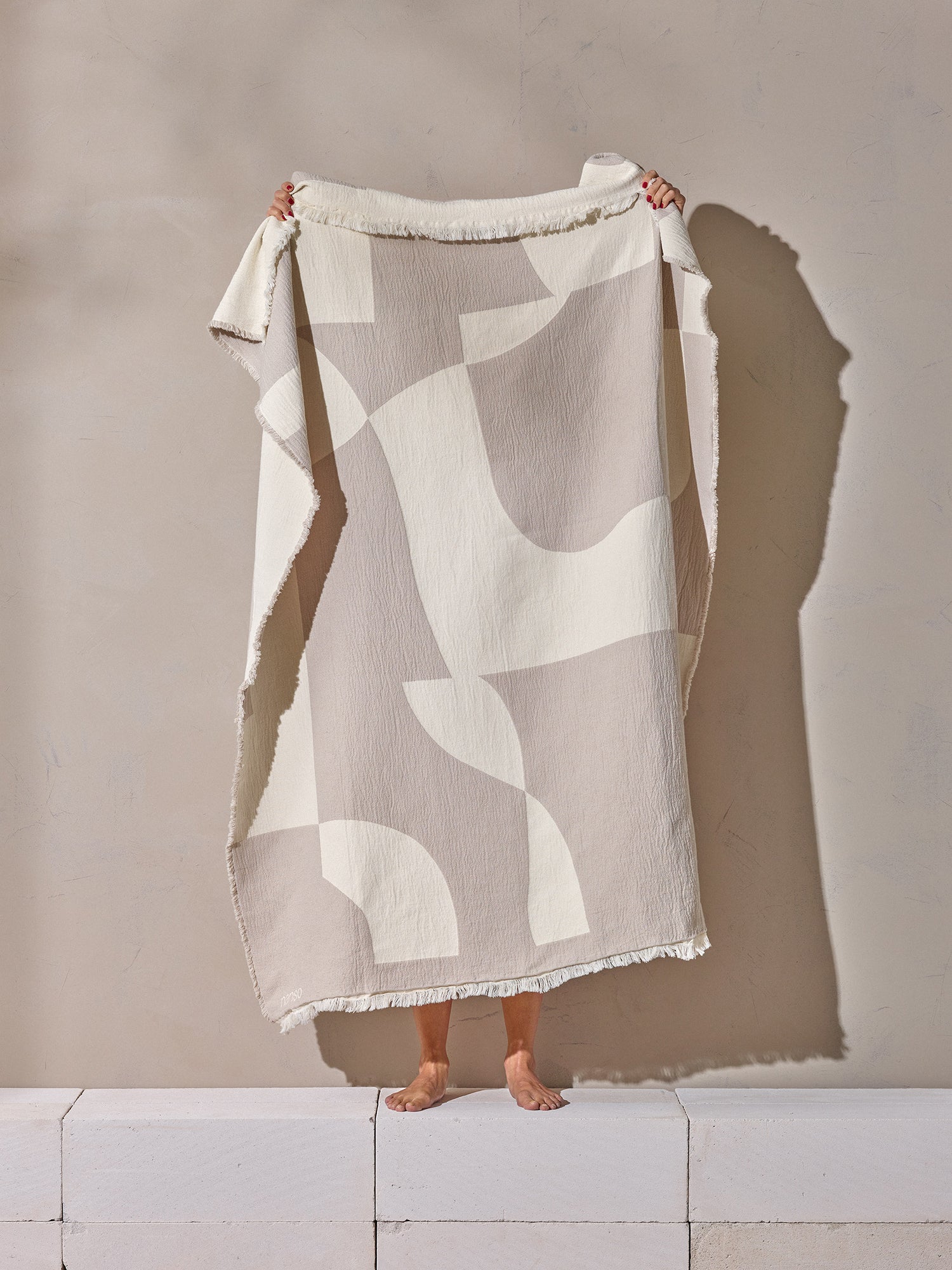 Beautiful Kallio blanket with a soft beige and white harmonious two-tone pattern. Crafted from cotton. Product picture with a woman holding the blanket.