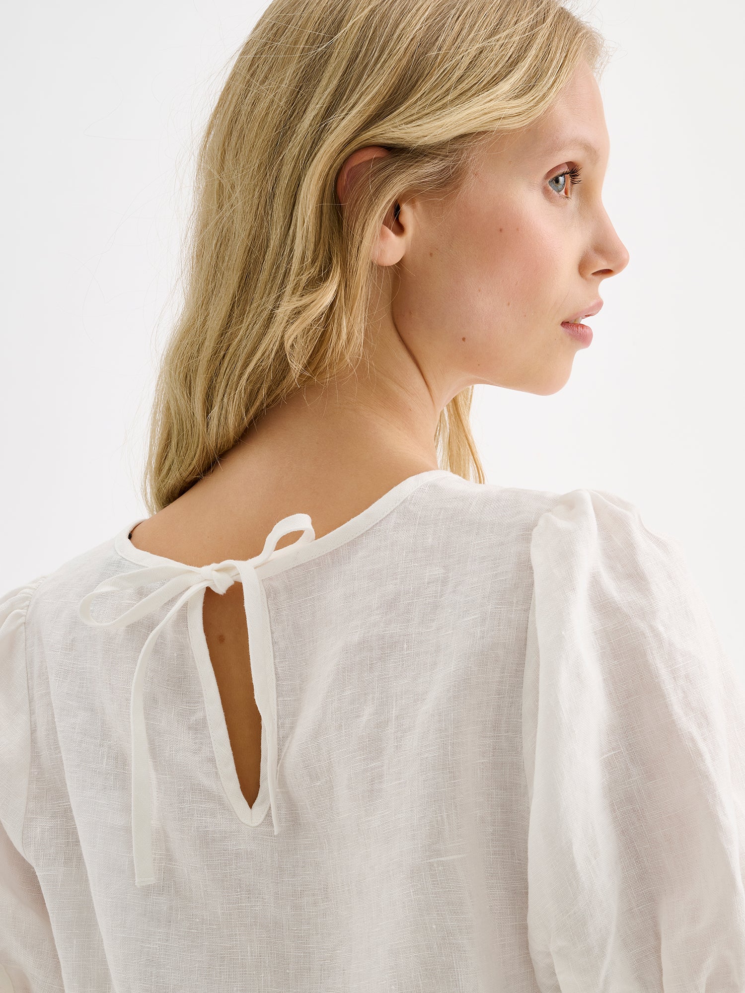 Nanso women's white breathable Sarastus linen blouse featuring short puffed sleeves on a model close-up pictured from the backside