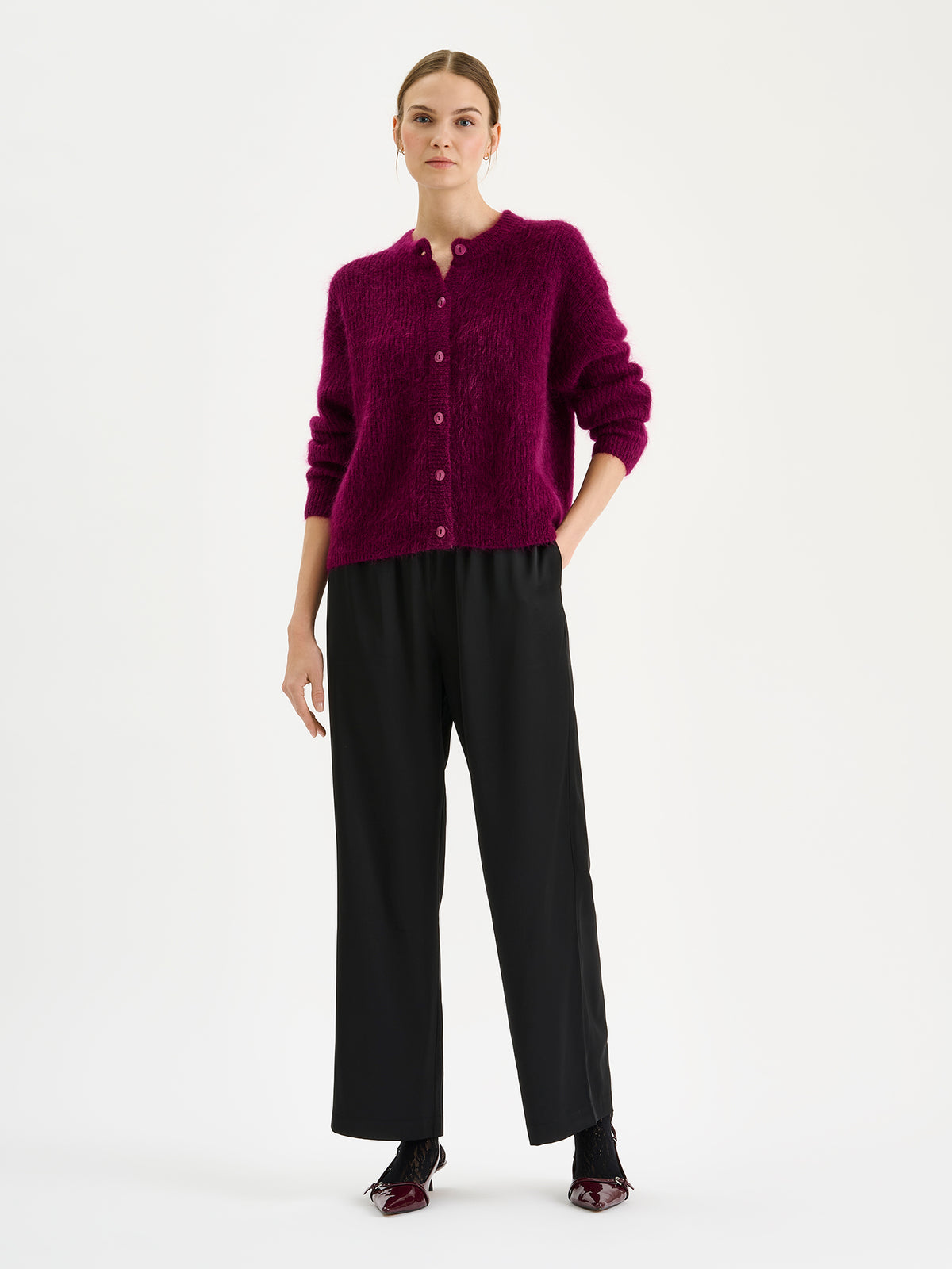 Nanso women's wonderfully warm and luxurious Sumi cardigan enchants with its vibrant violet hue and beautifully fluffy texture, pictured on a model with black trousers.