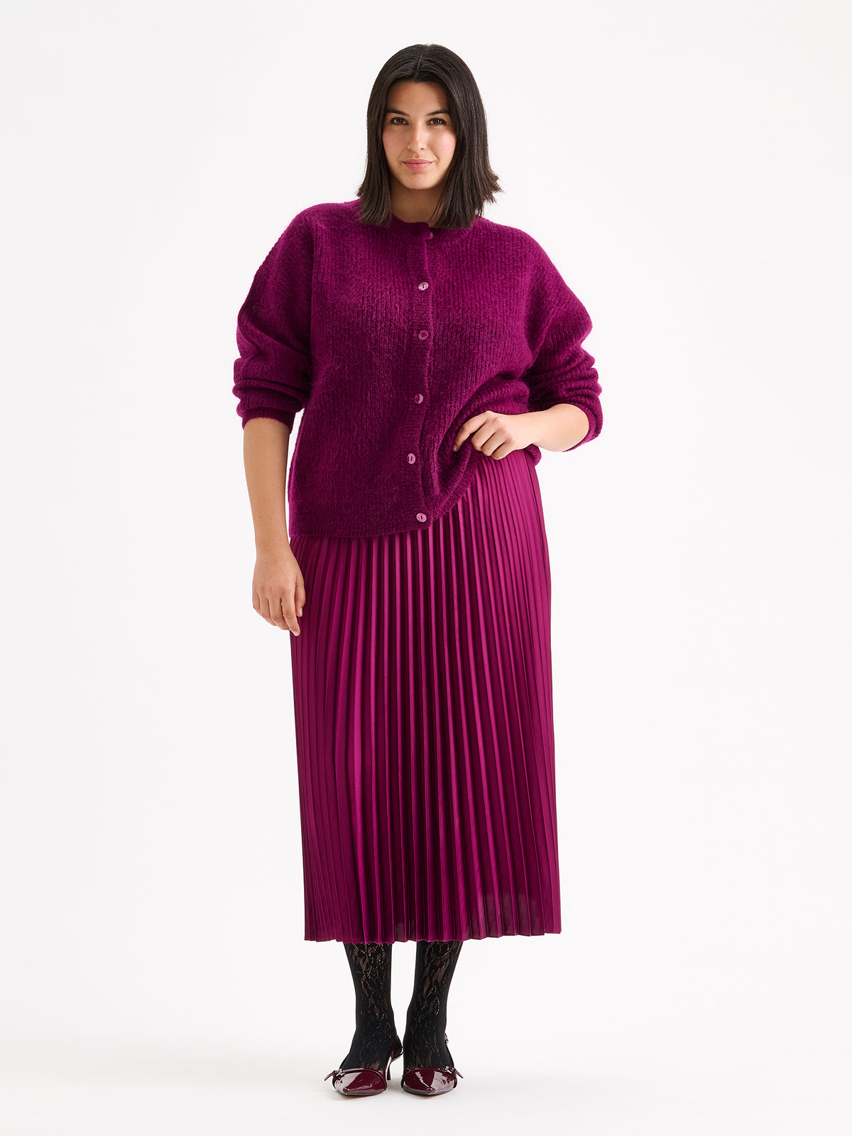 Nanso women's wonderfully warm and luxurious Sumi cardigan enchants with its vibrant violet hue and beautifully fluffy texture, pictured on a model with a pleated skirt.