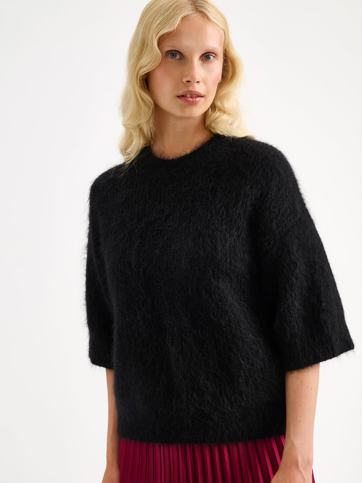 Nanso women's wonderfully warm and luxurious Sumi knitted sweater in classic black and beautifully fluffy texture. Pictured on a model with a violet pleated skirt.
